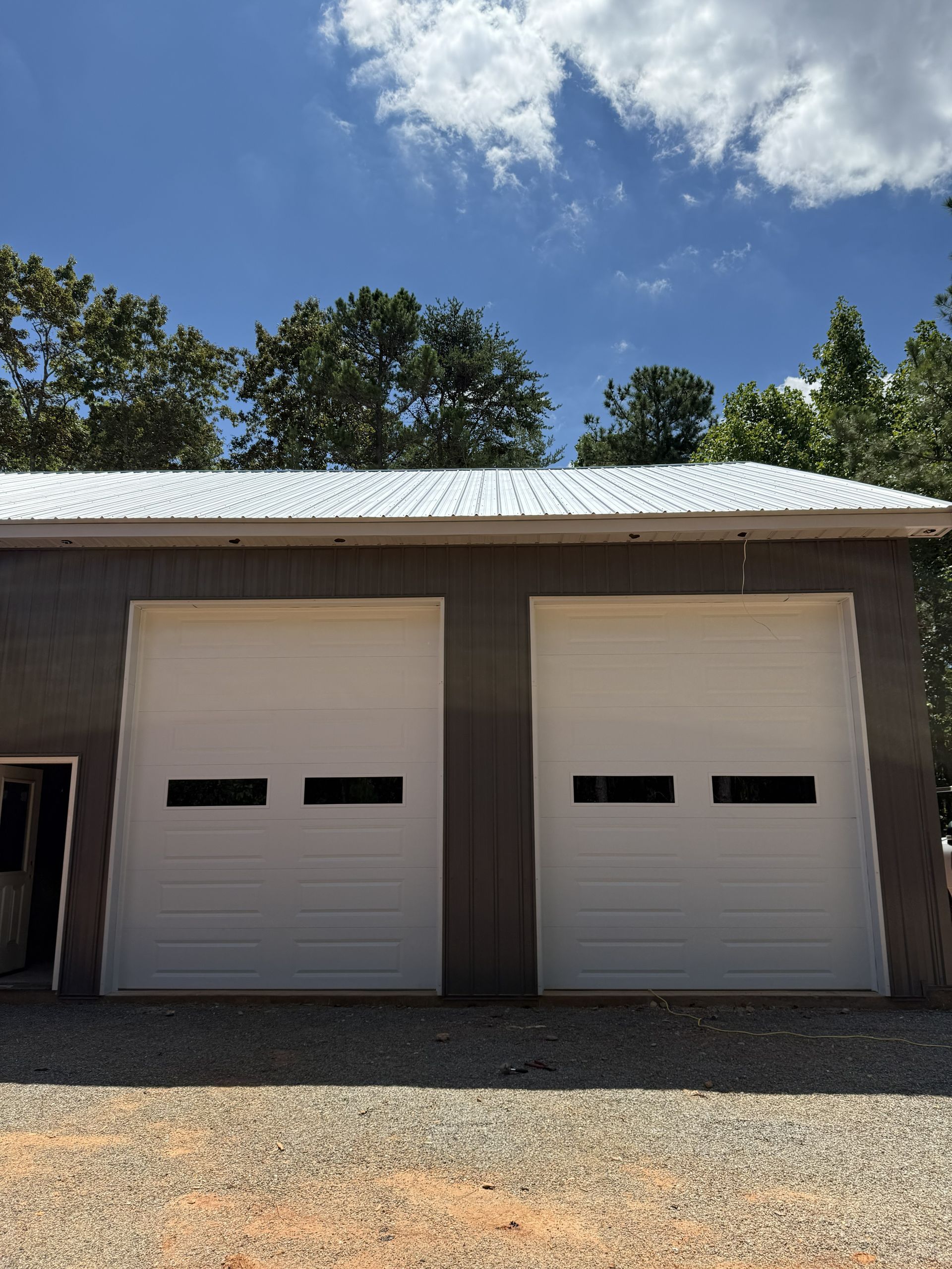 Two white garage doors on a gray building with a metal roof against a sunny sky.