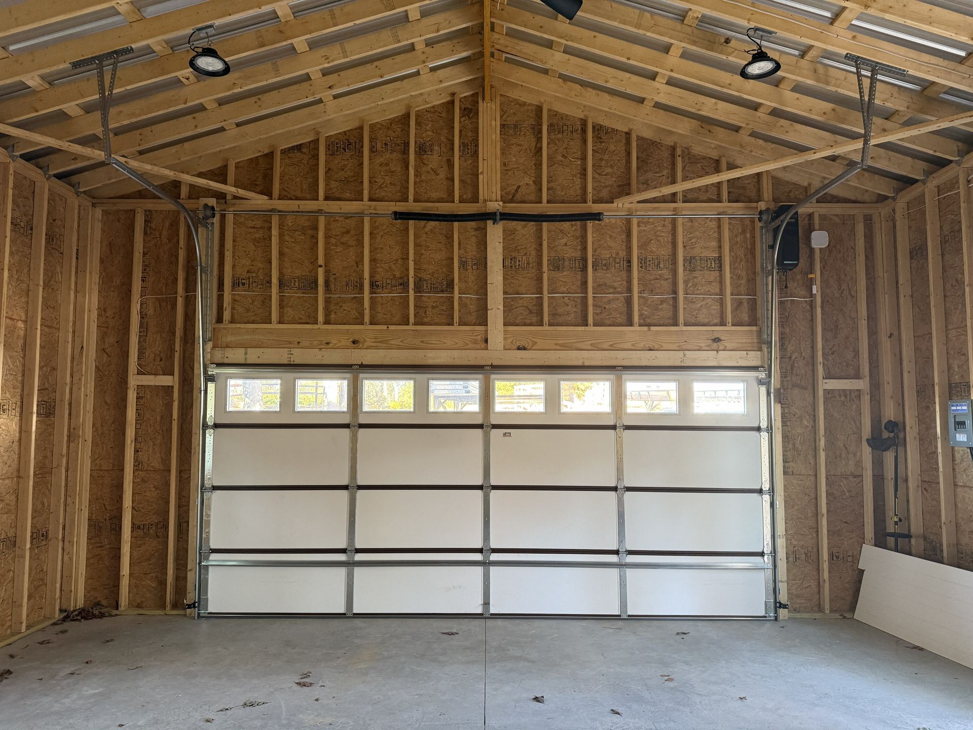 Interior of an unfinished garage with a closed, light-colored garage door. Wooden framework visible.