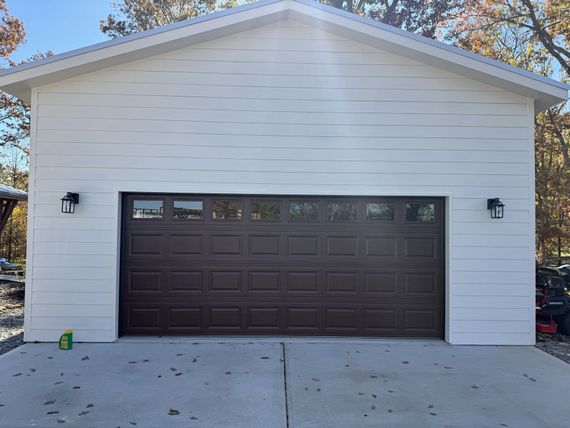 White-sided garage with brown garage door, two black lights, concrete driveway, and a blue sky in the background.