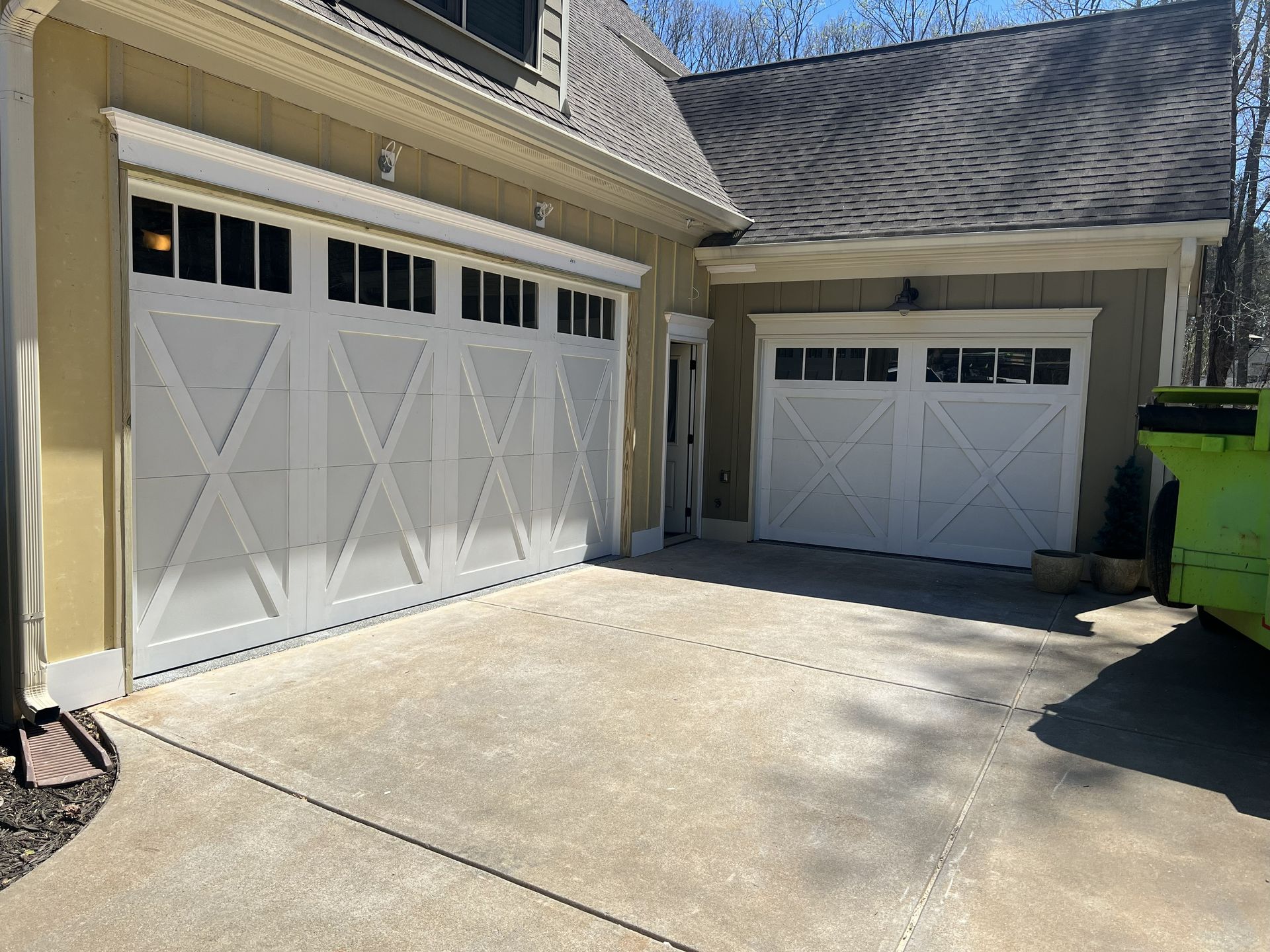 White garage doors on a light beige house. Concrete driveway with a dumpster.