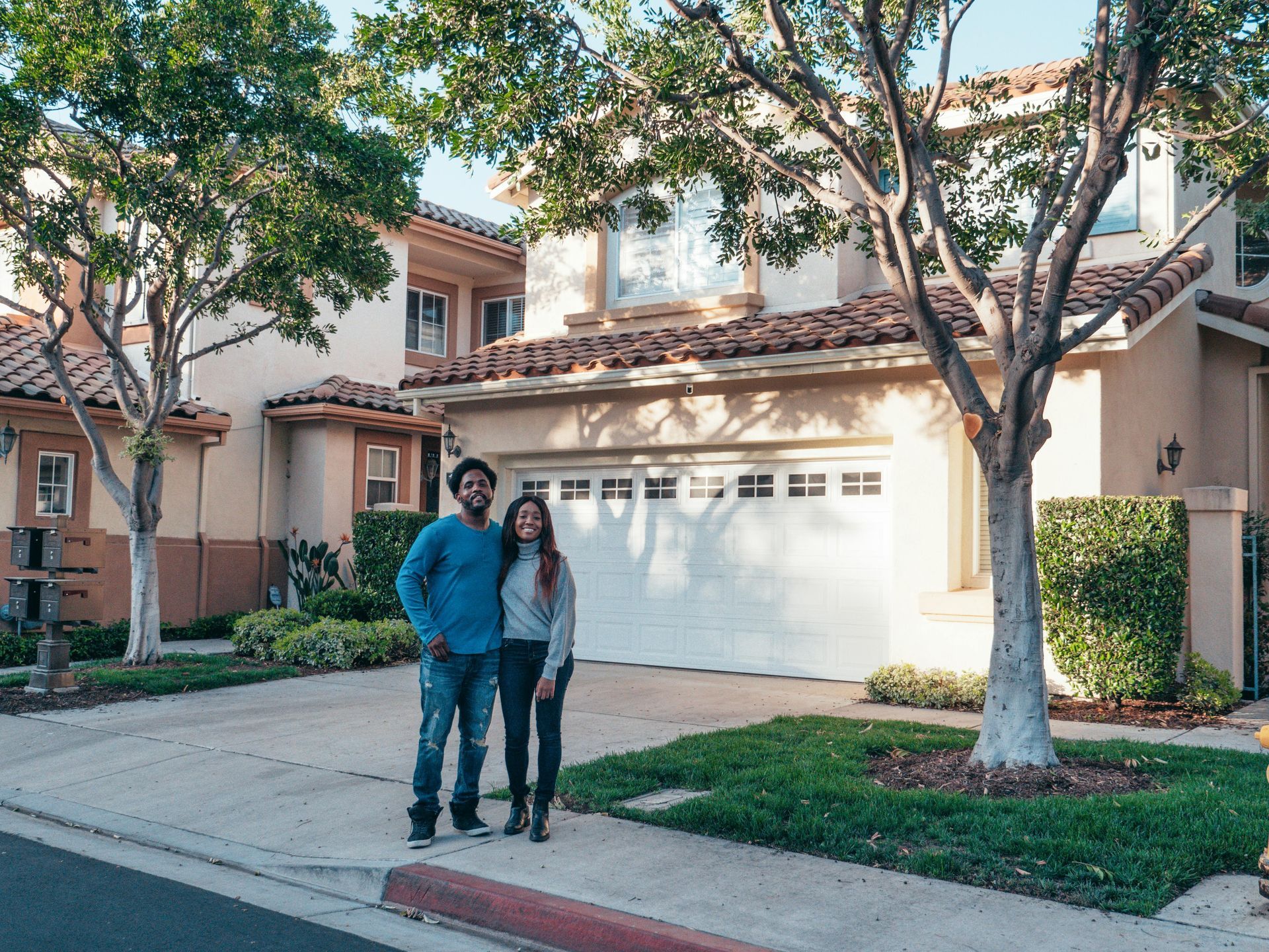 Couple standing in front of their new house; a two-story beige home with a garage and green lawn.