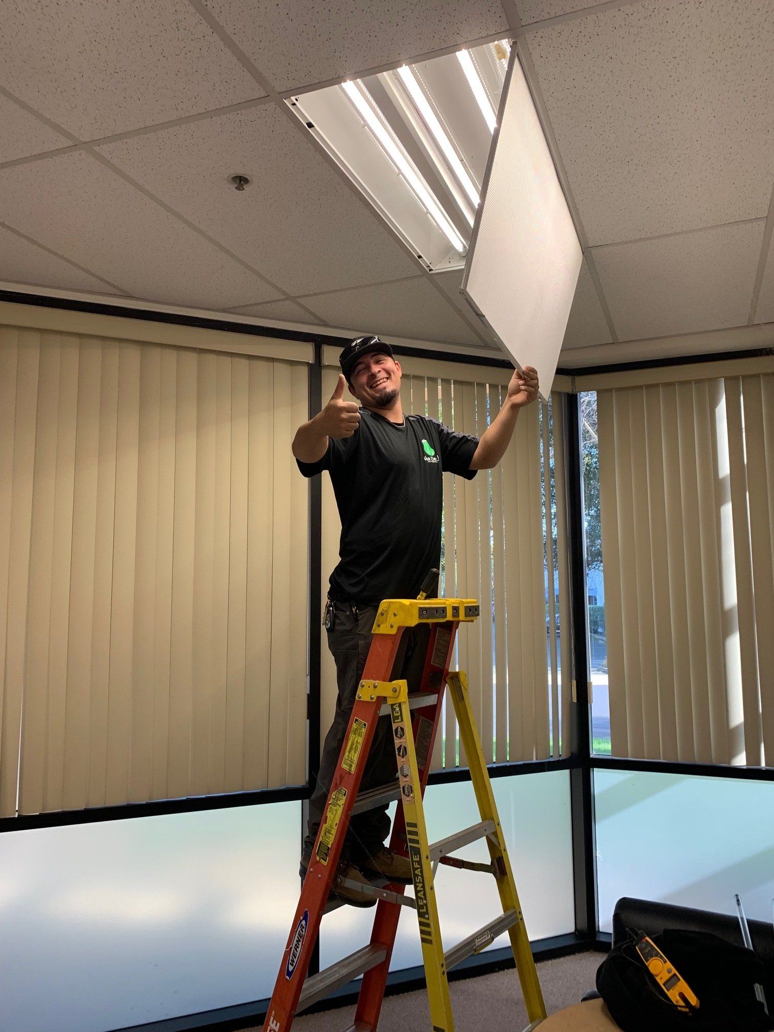 A man is standing on a ladder fixing a light fixture.