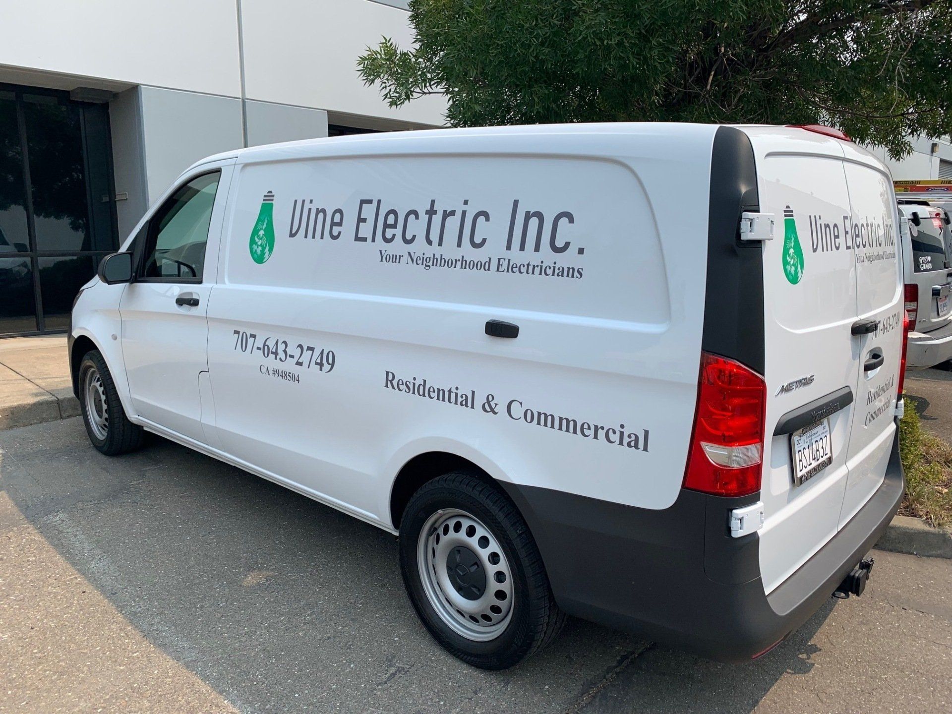 A white van with vine electric inc. written on the side is parked in front of a building.