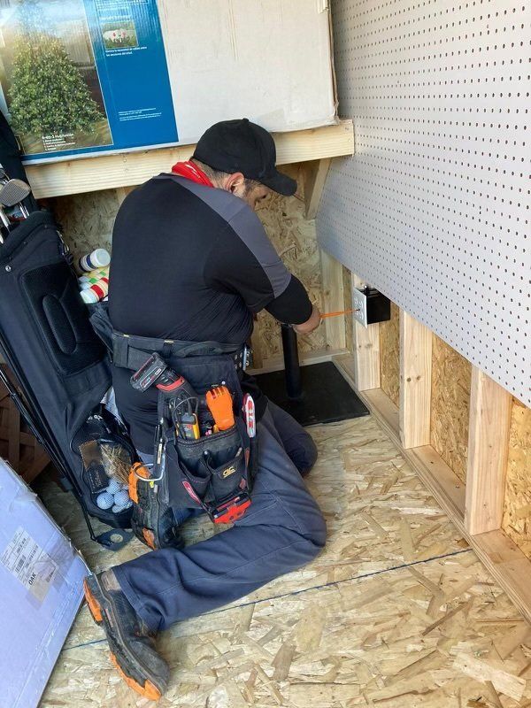 A man is kneeling down in a shed working on a pipe.