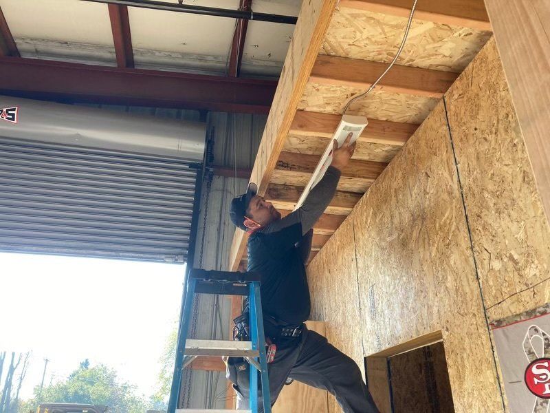 A man is standing on a ladder working on the ceiling of a building.