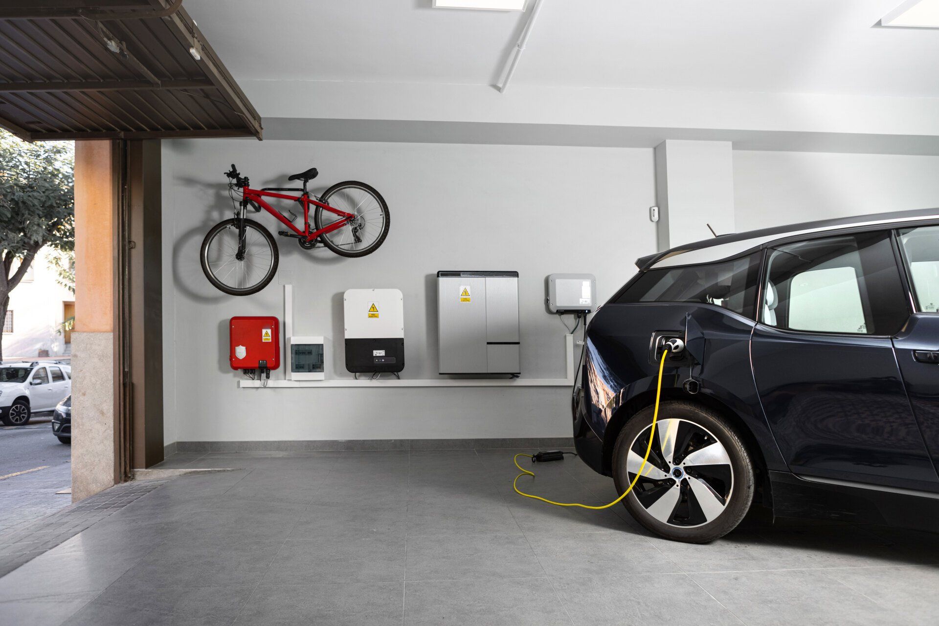 A car is being charged in a garage with a bicycle hanging on the wall.