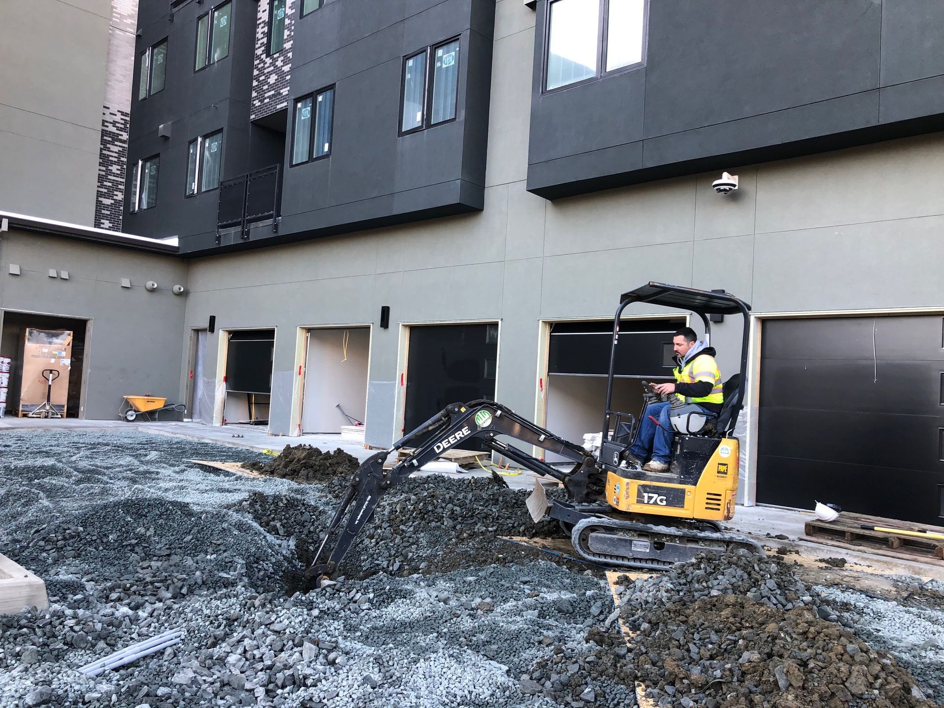 A man is driving a small excavator in front of a building.