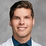 A man in a white coat and tie is smiling for the camera.