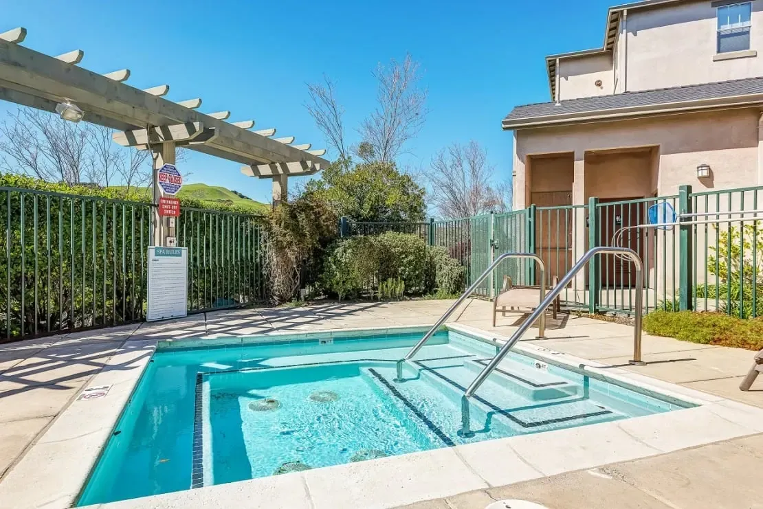 Outdoor hot tub with steps and handrails, surrounded by a fence.