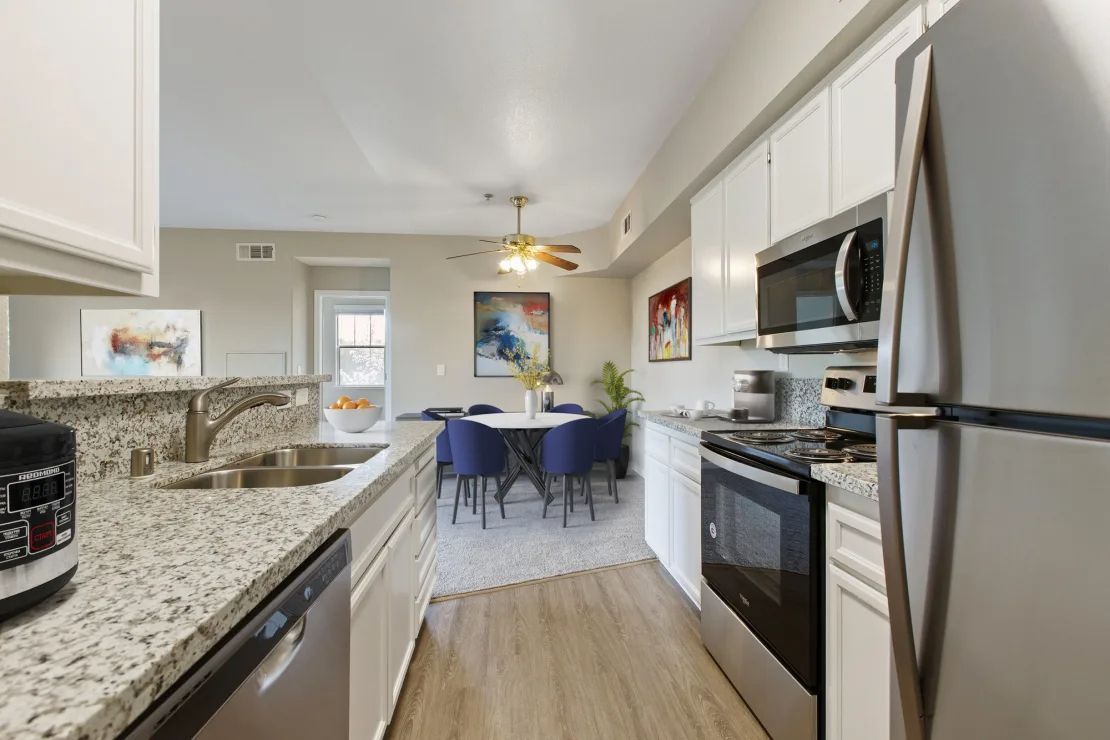 Bright kitchen with granite counters, stainless appliances, and a dining nook with blue chairs.