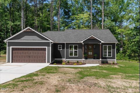 Gray single-story house with a two-car garage, front porch, and wooded yard