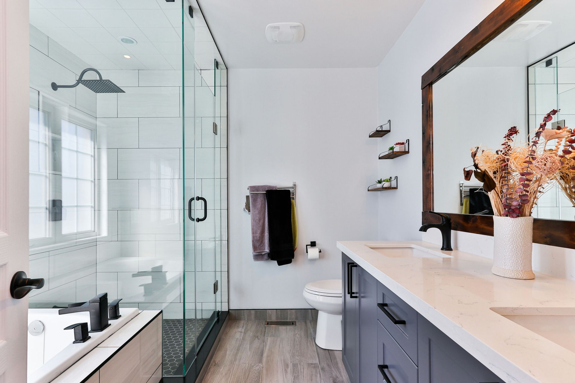 Modern bathroom with glass shower, white walls, dark vanity, and a large mirror with flowers