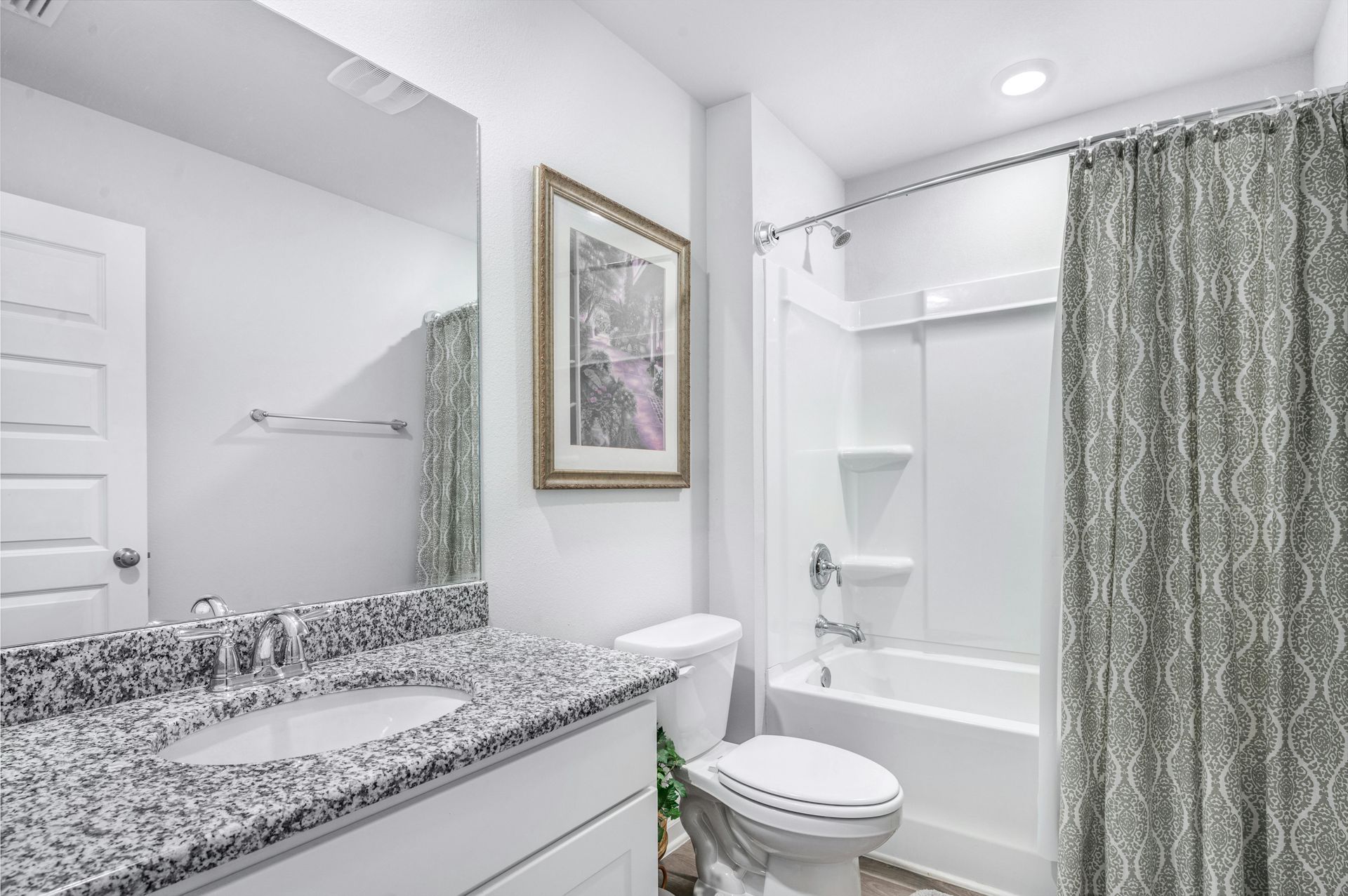 Bright bathroom with granite vanity, toilet, tub, and gray shower curtain