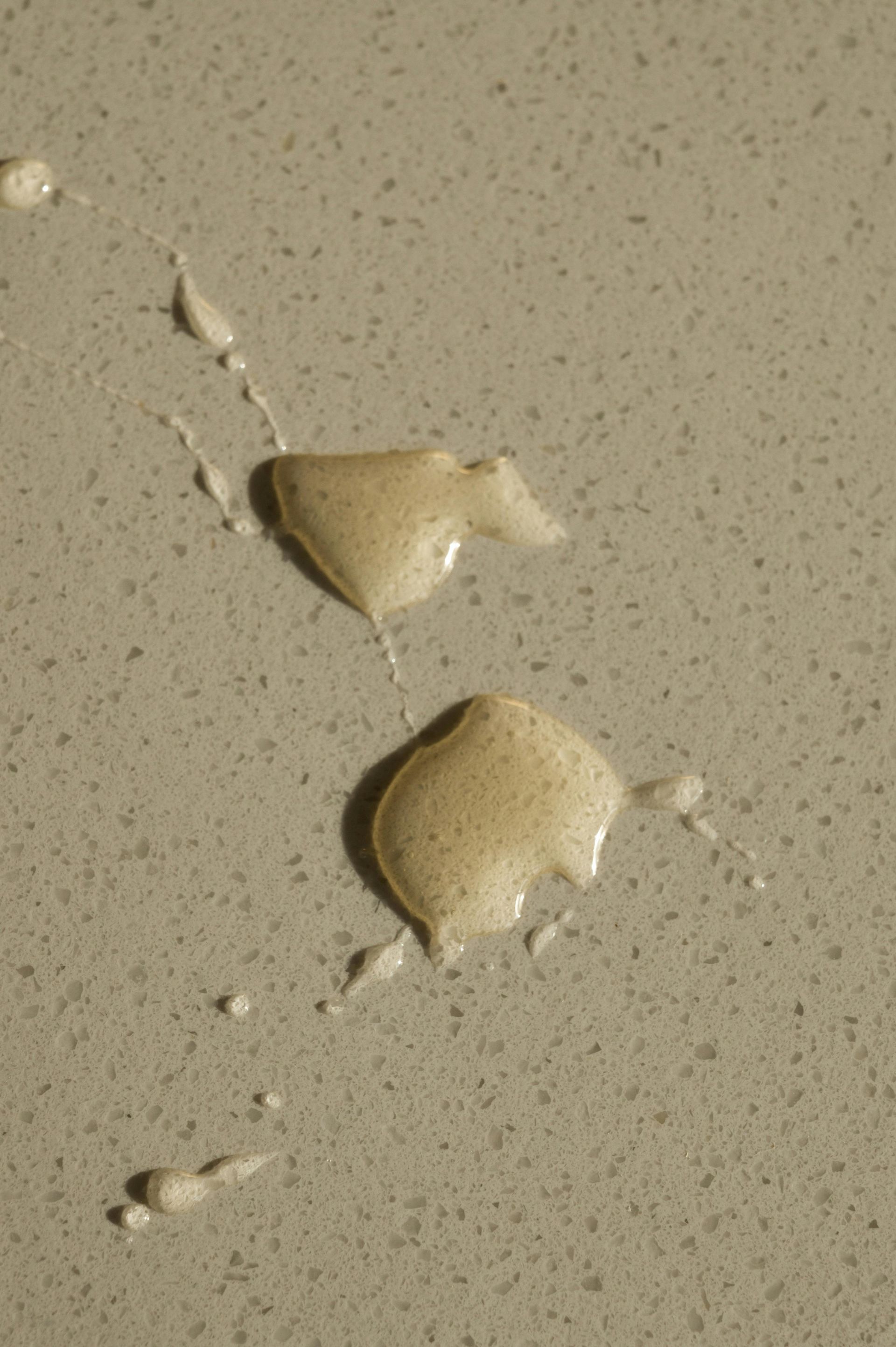 Two beige drops of sauce on a speckled countertop