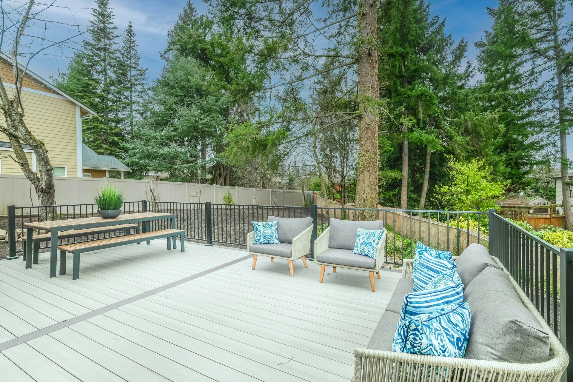 Backyard deck with wicker seating, picnic table, and trees beyond the fence
