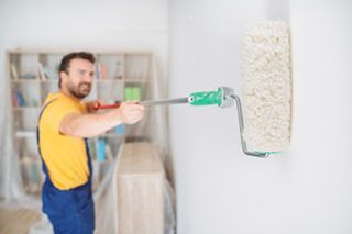 A man is painting a wall with a paint roller.