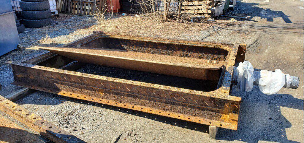 Two rusty metal pieces are sitting on top of a gravel road.