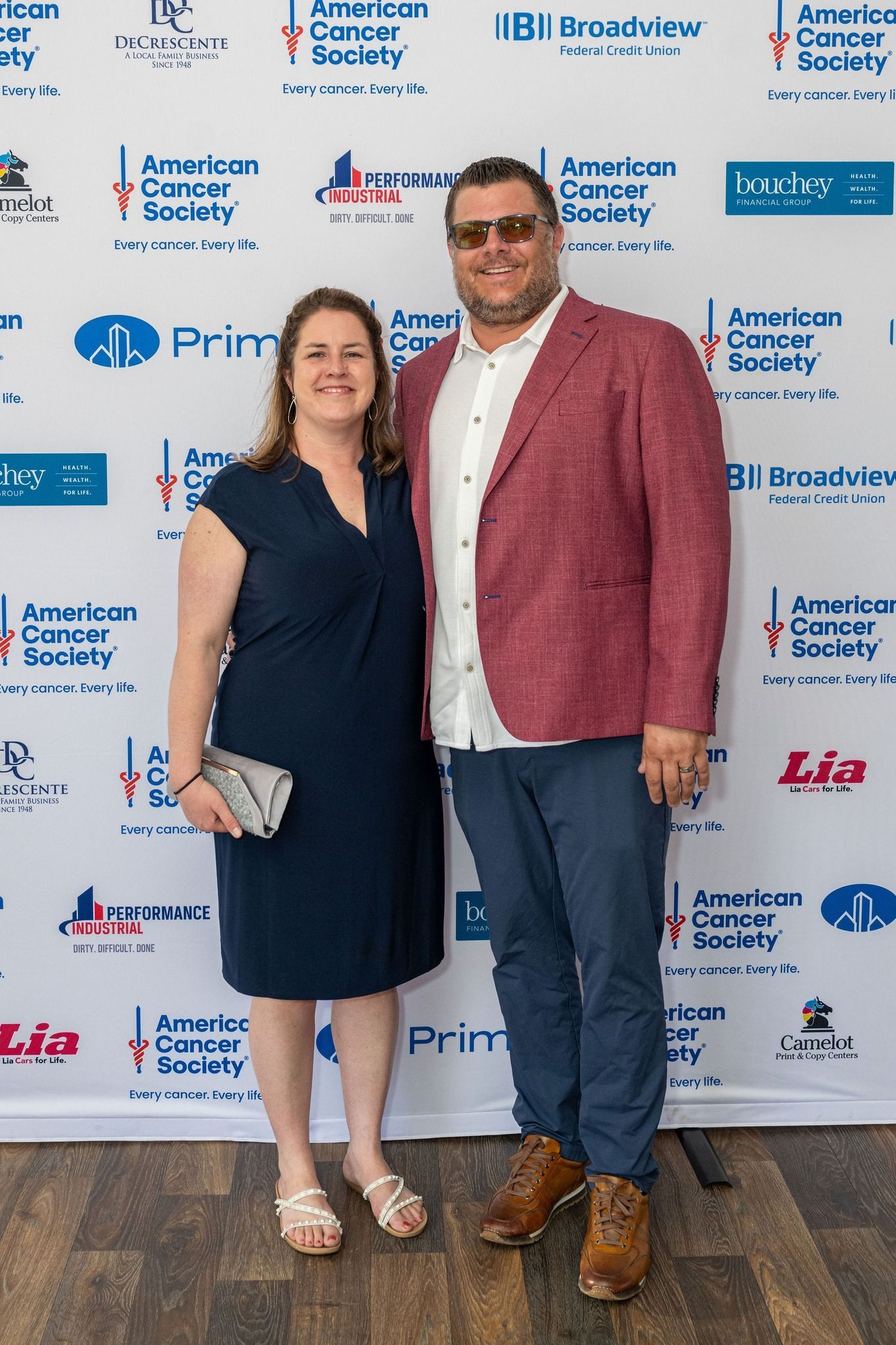 A couple representing Performance Industrial are posing for a picture in front of a wall