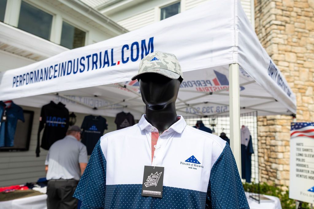 A mannequin wearing a blue and white polo shirt is standing under a performance industrial tent.