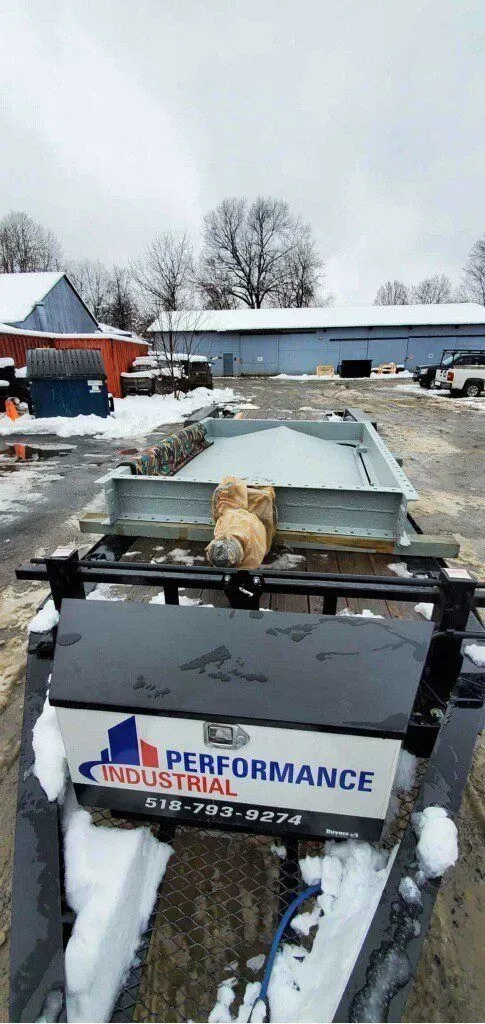 A dog is sitting on the back of a tractor in the snow.