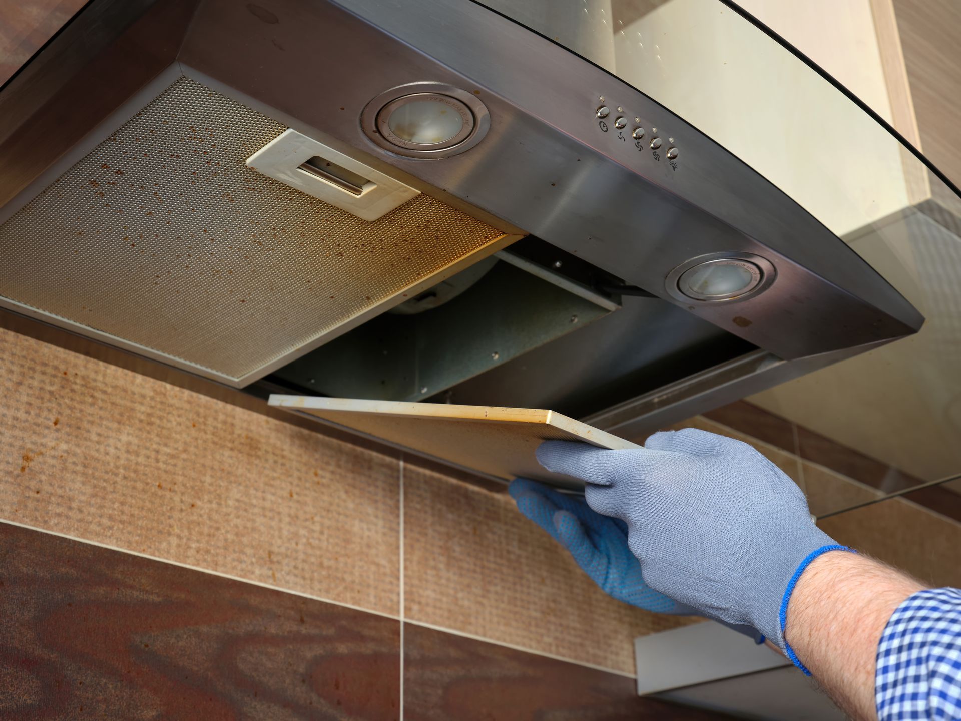 Person with gloved hands removing a greasy kitchen range hood filter.