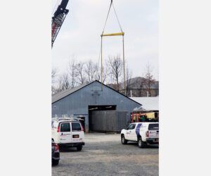 A crane is lifting a large object over a building in a parking lot.