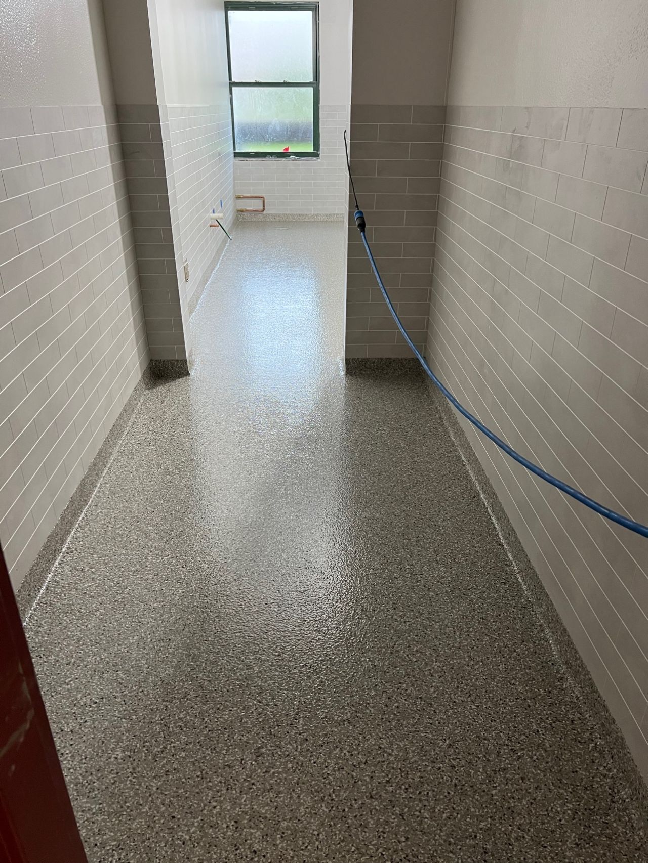 A long hallway with a hose attached to the wall and a window.