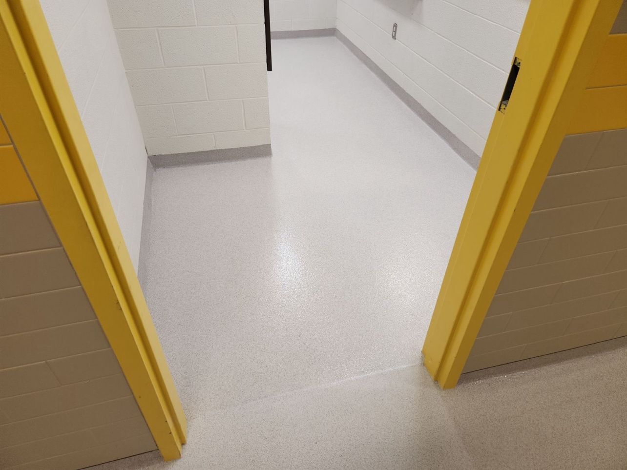 A hallway with a white floor and yellow trim between two doors.