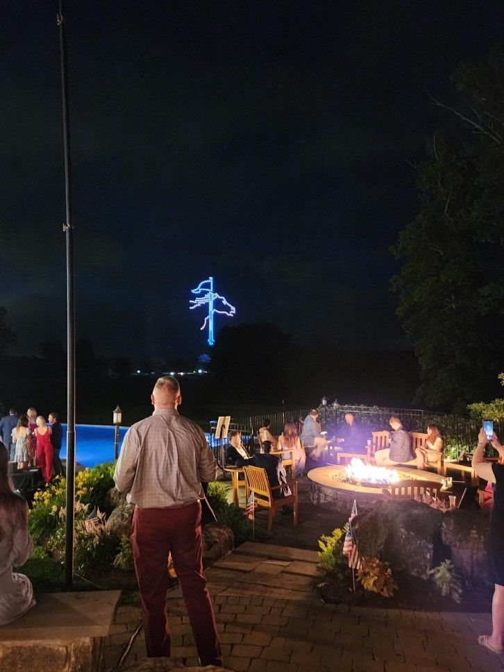 A group of people are standing around a fire pit at night.