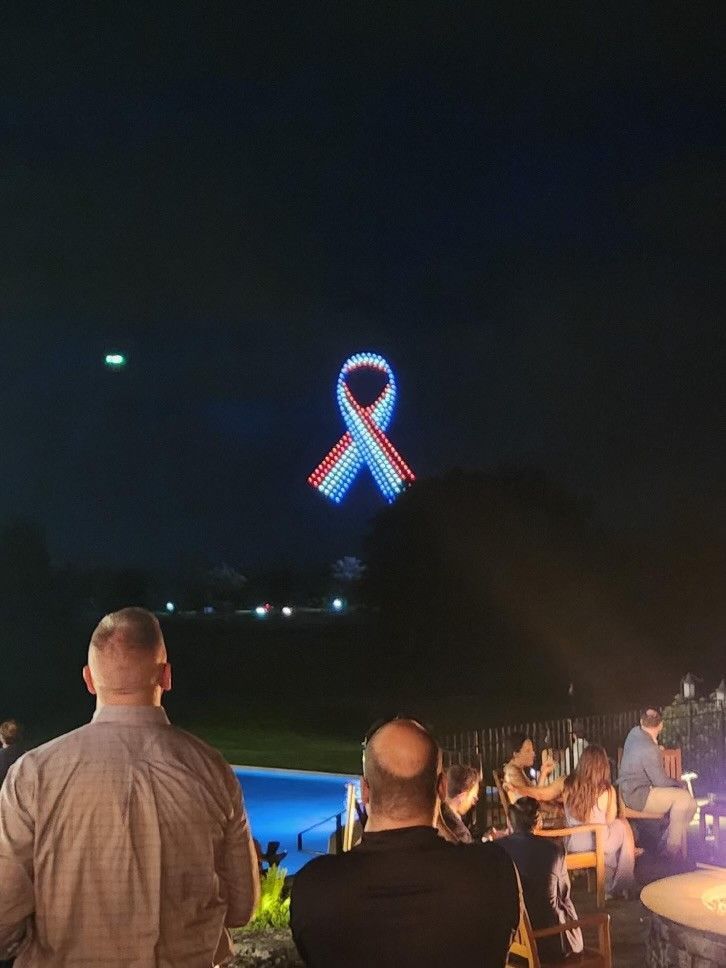 A group of people are watching a fireworks display with a ribbon in the sky.