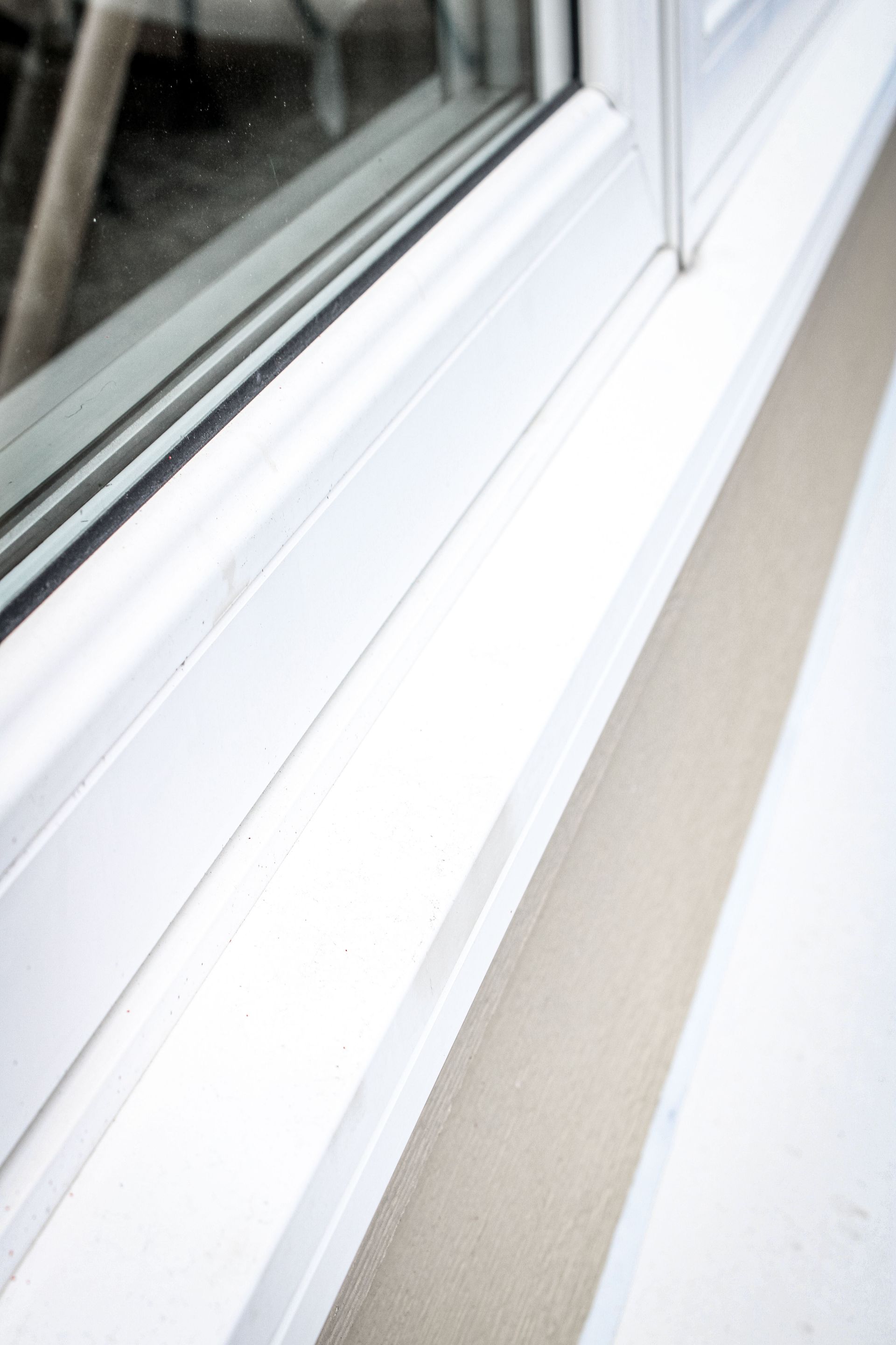 A close up of a white window sill with a sliding glass door.