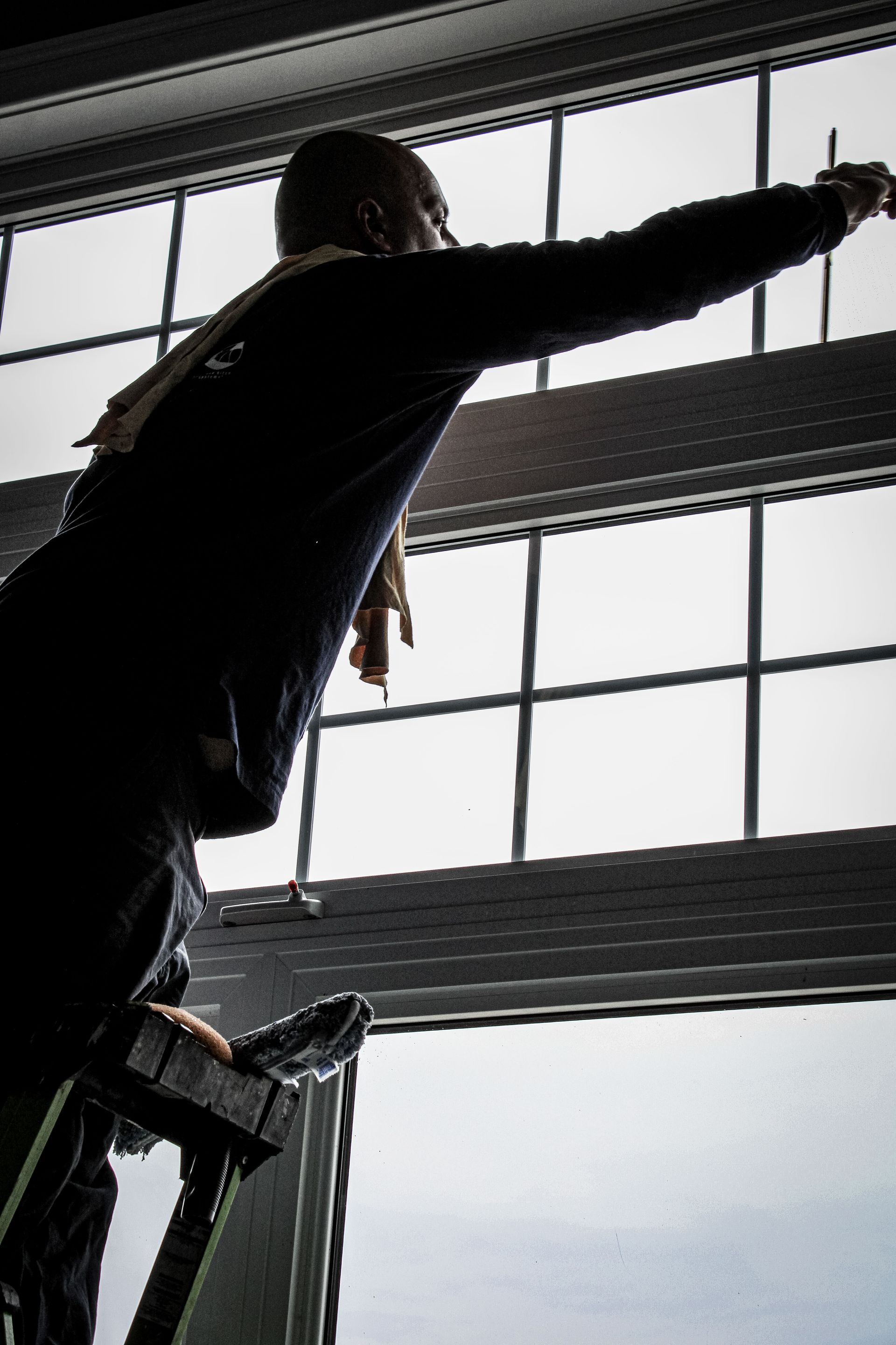 A man is standing on a ladder looking out a window.