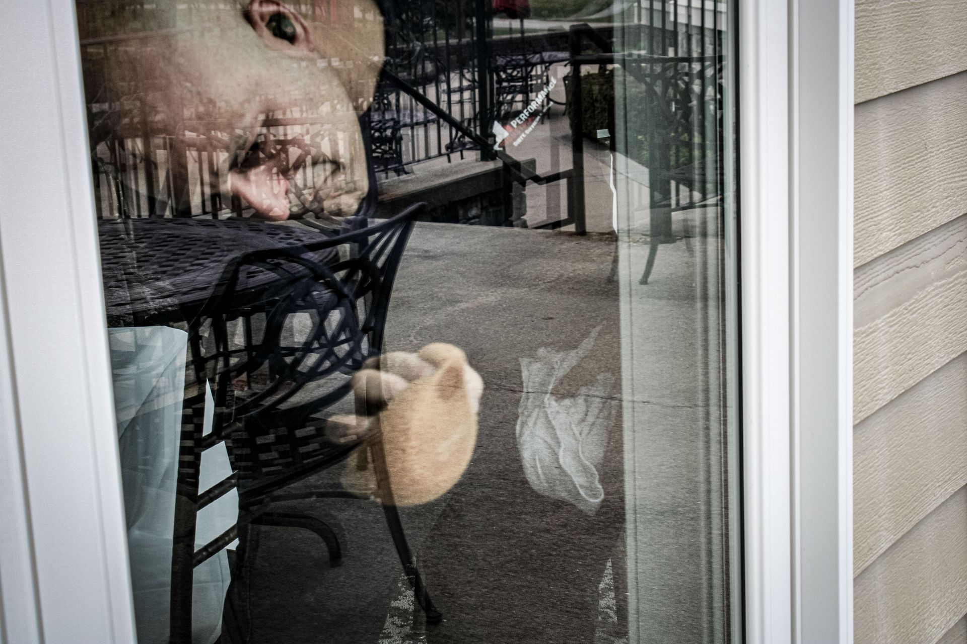 A man is sitting at a table with a teddy bear behind a glass door.