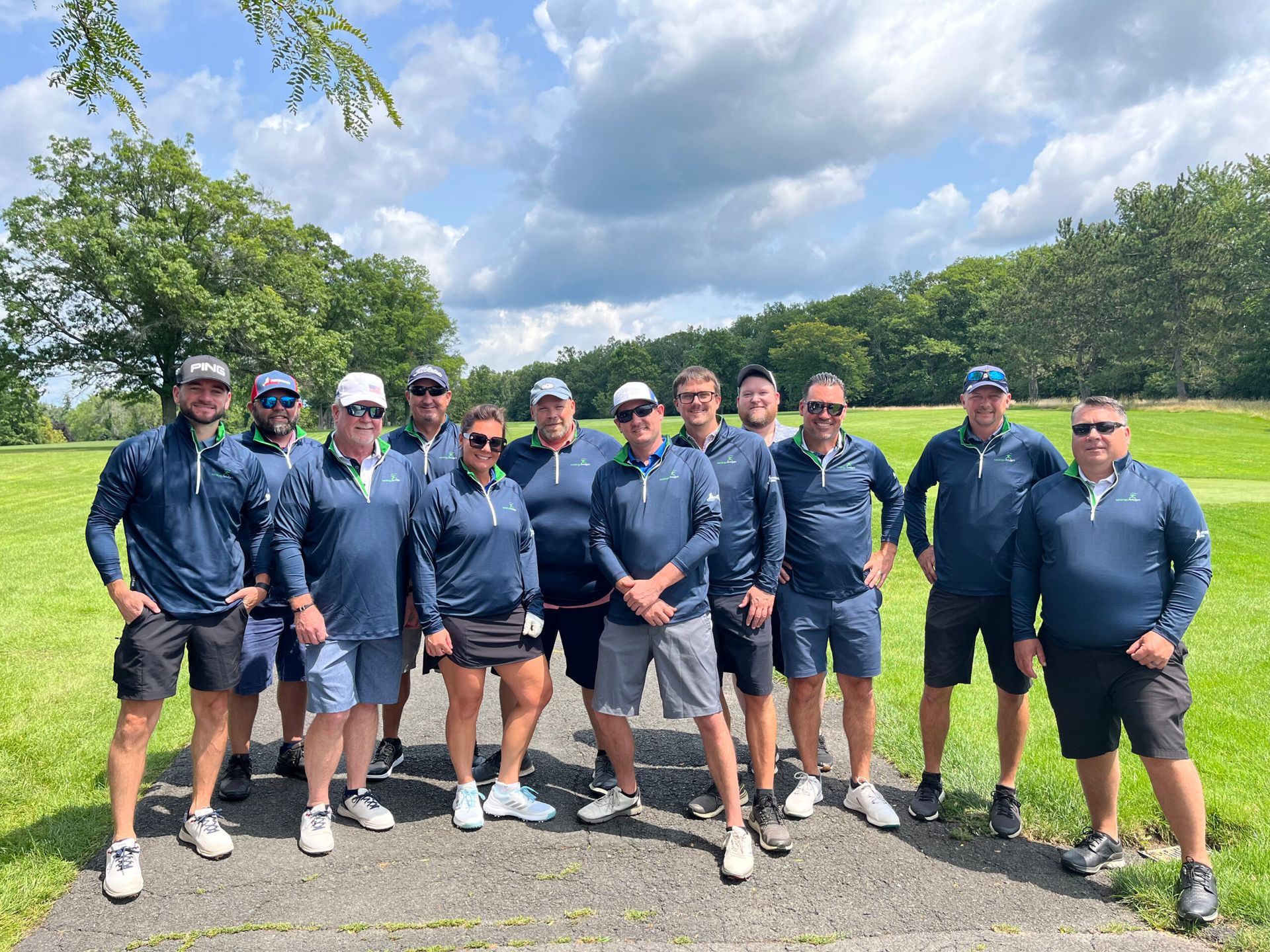 A group of people are posing representing the company for a picture on a golf course.