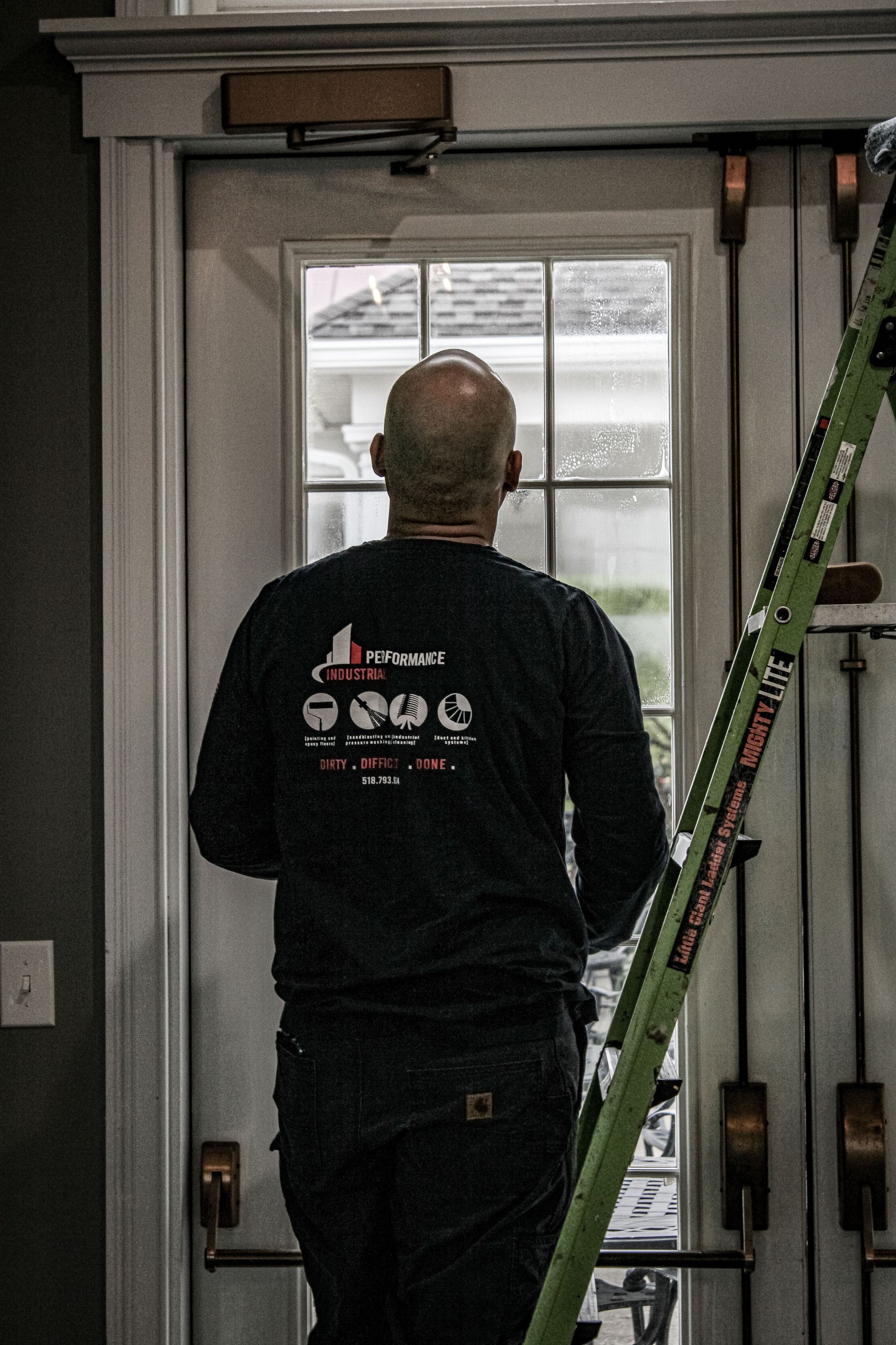 A man is standing on a ladder looking out of a door.