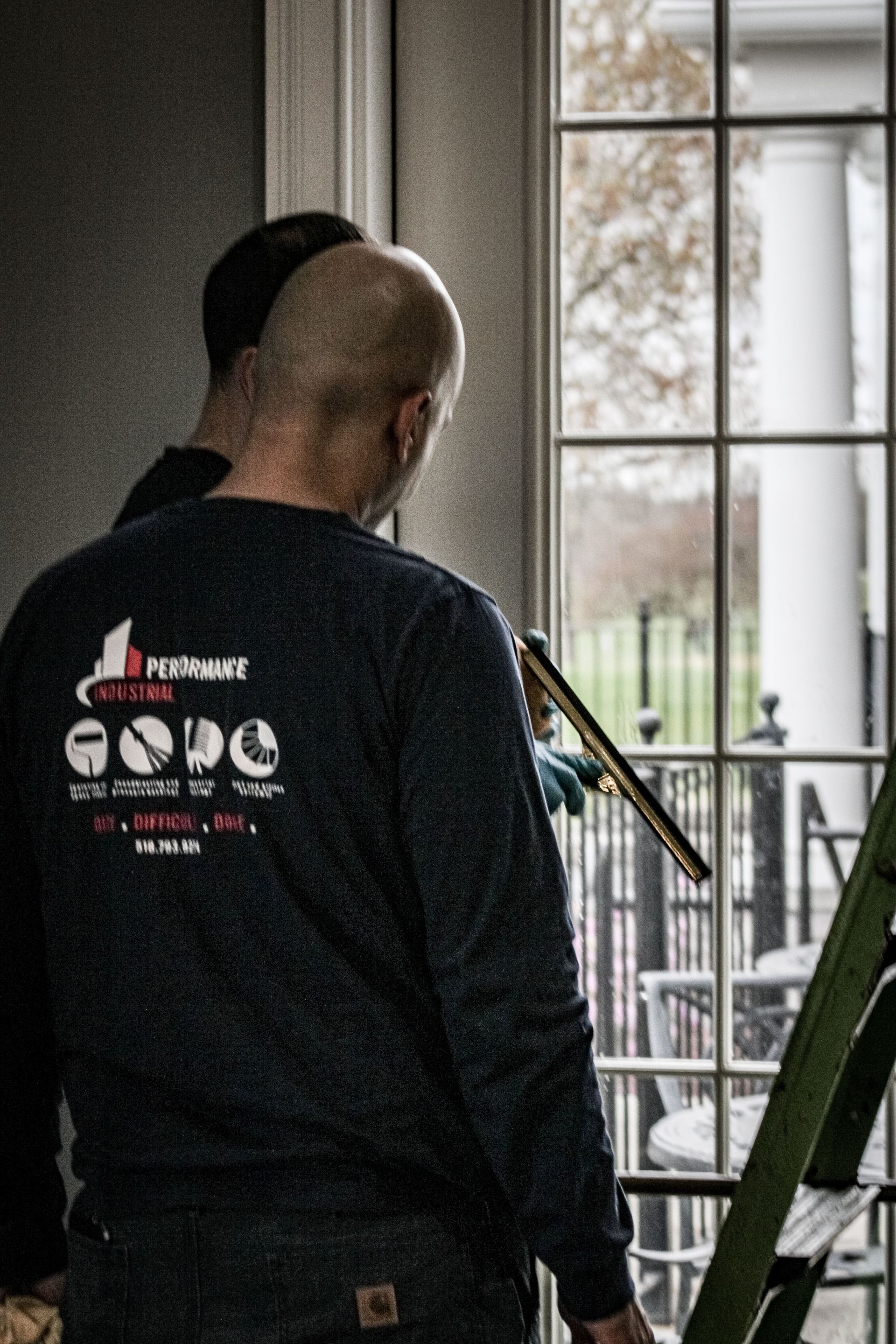 A man is cleaning a window with a ladder in the background.