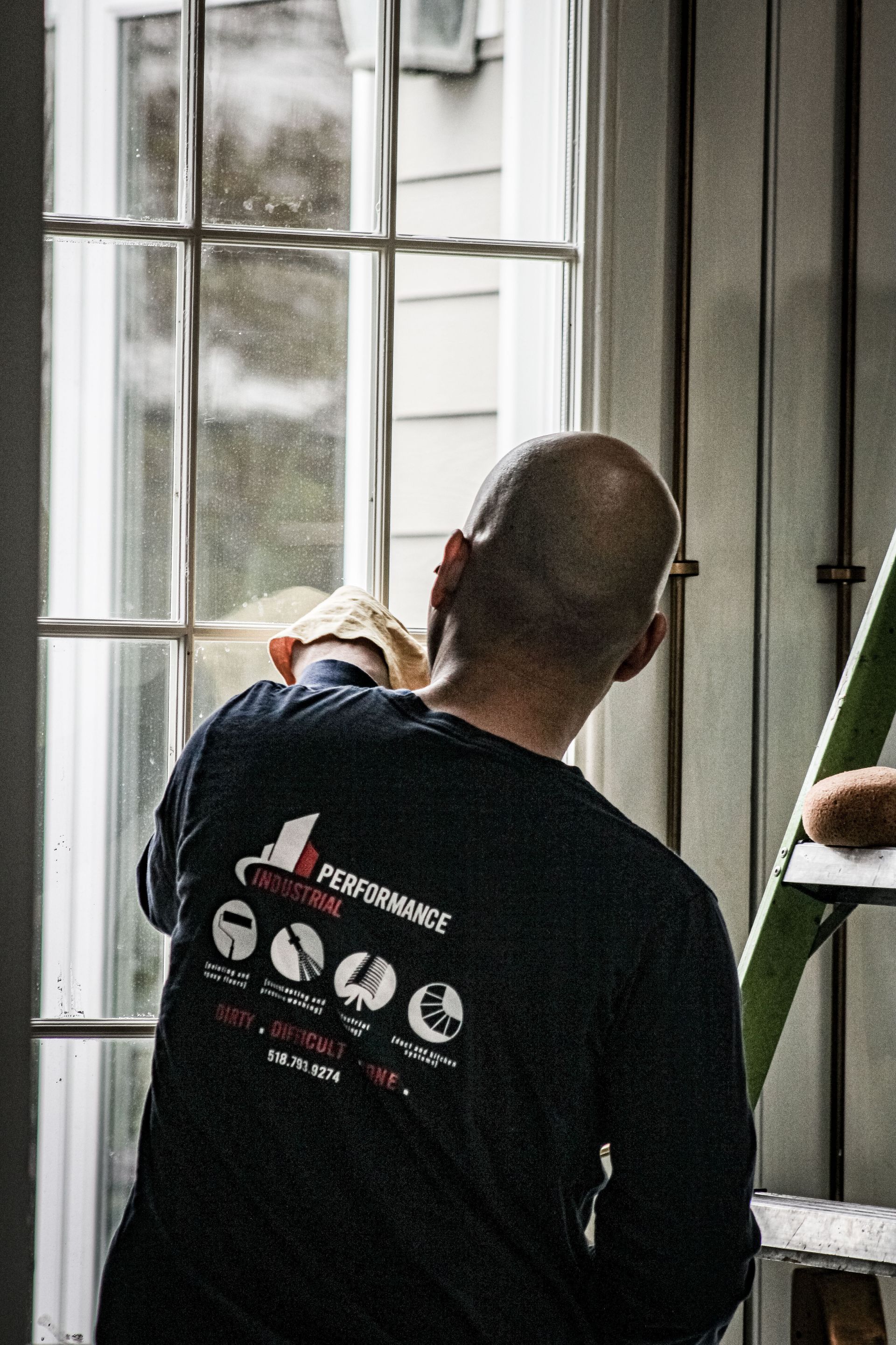 A man is standing on a ladder cleaning a window.