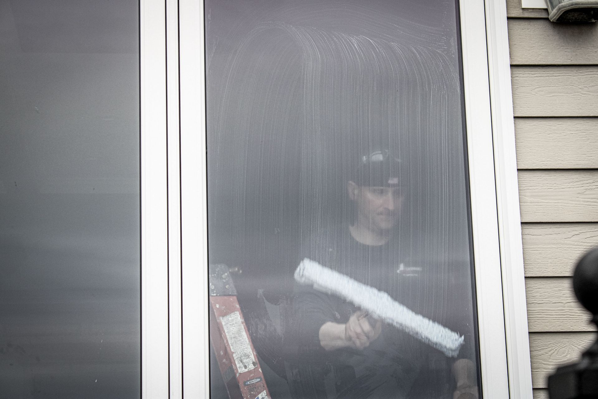 A man is cleaning a window with a ladder in the rain.