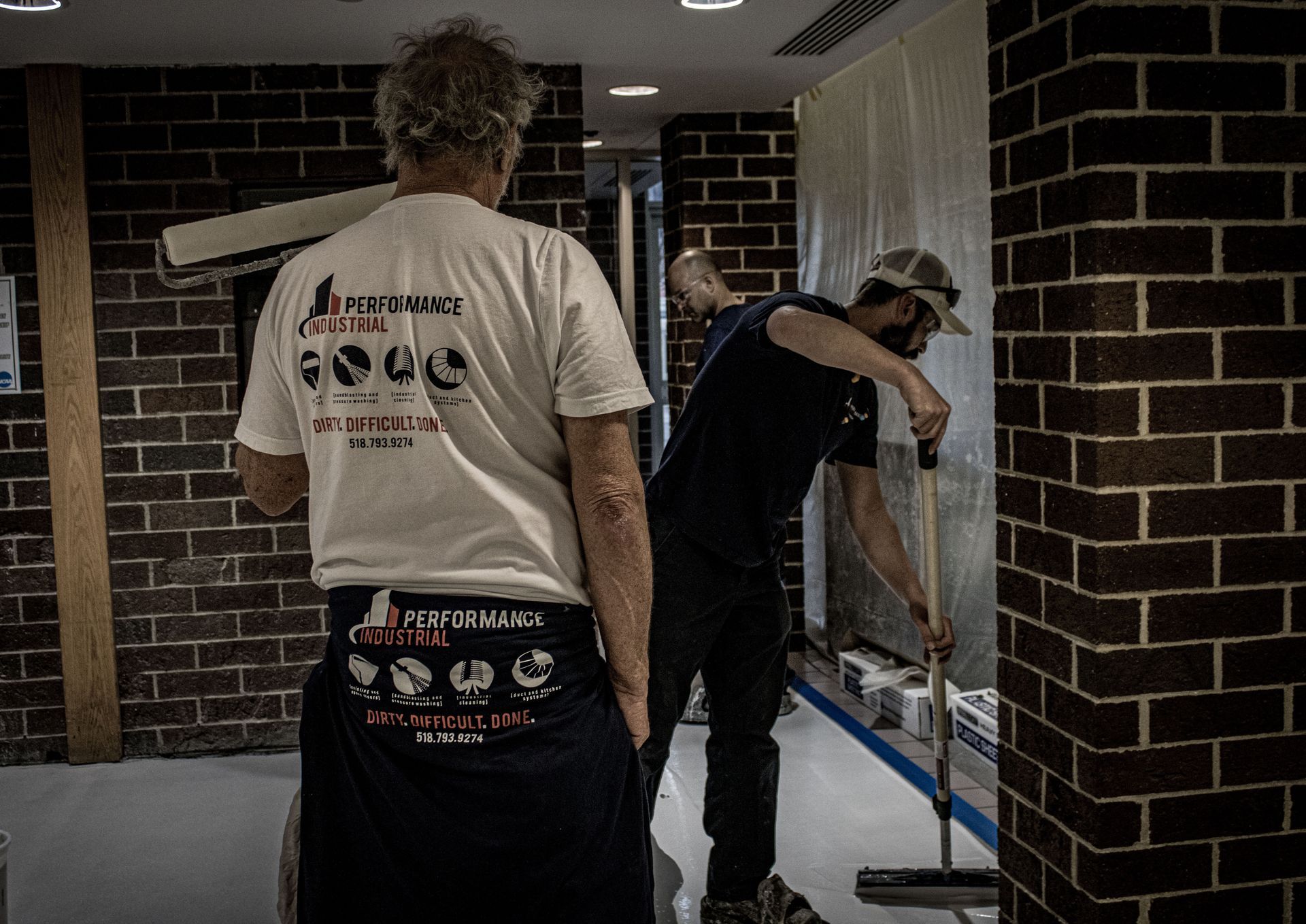 Two men are standing next to each other in front of a brick wall.