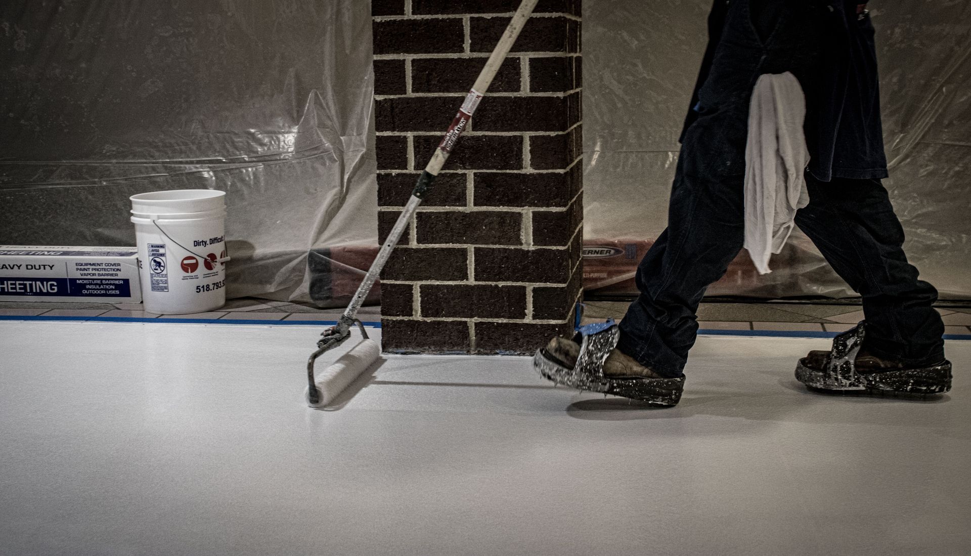 A person is painting a brick wall with a roller.