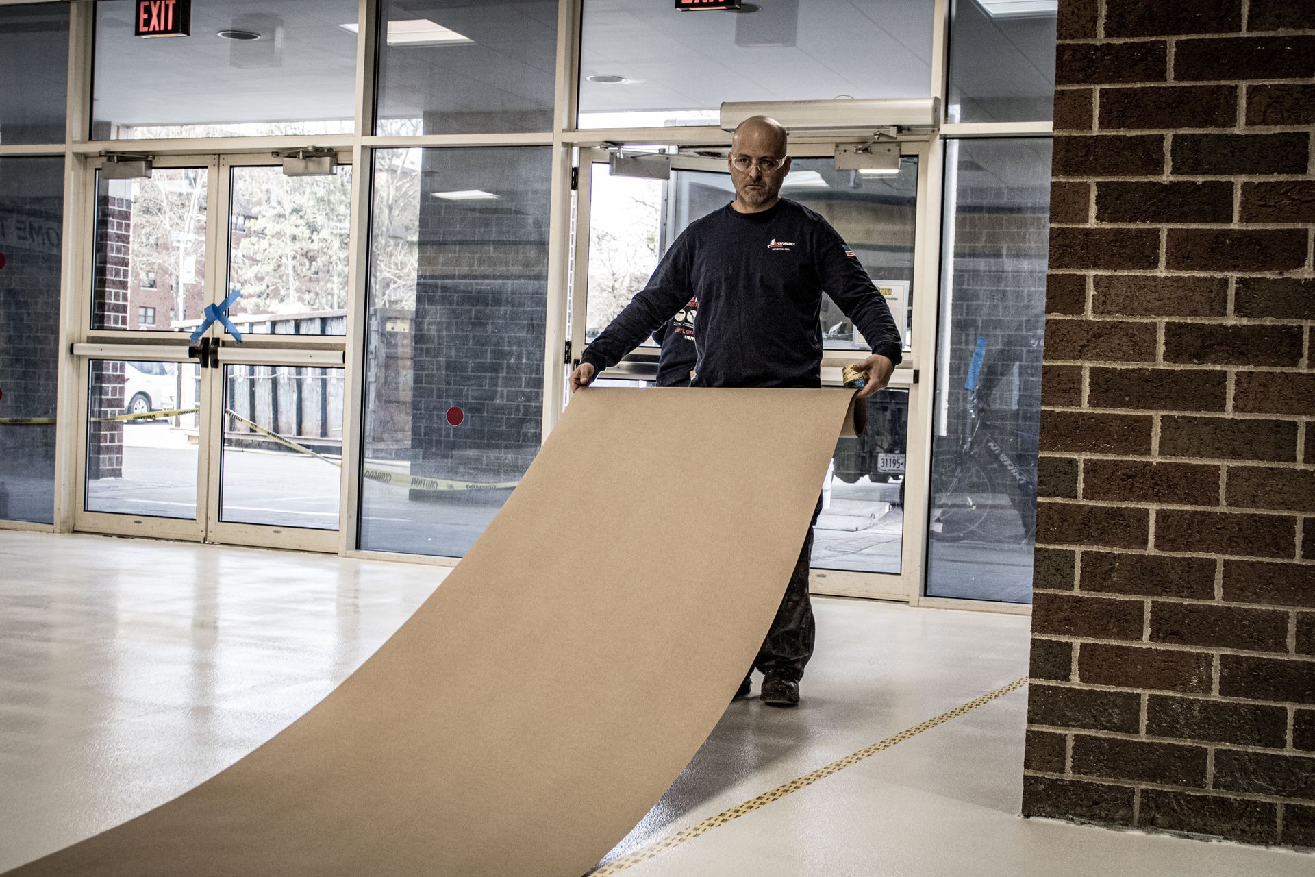 A man is carrying a large piece of cardboard in a hallway.