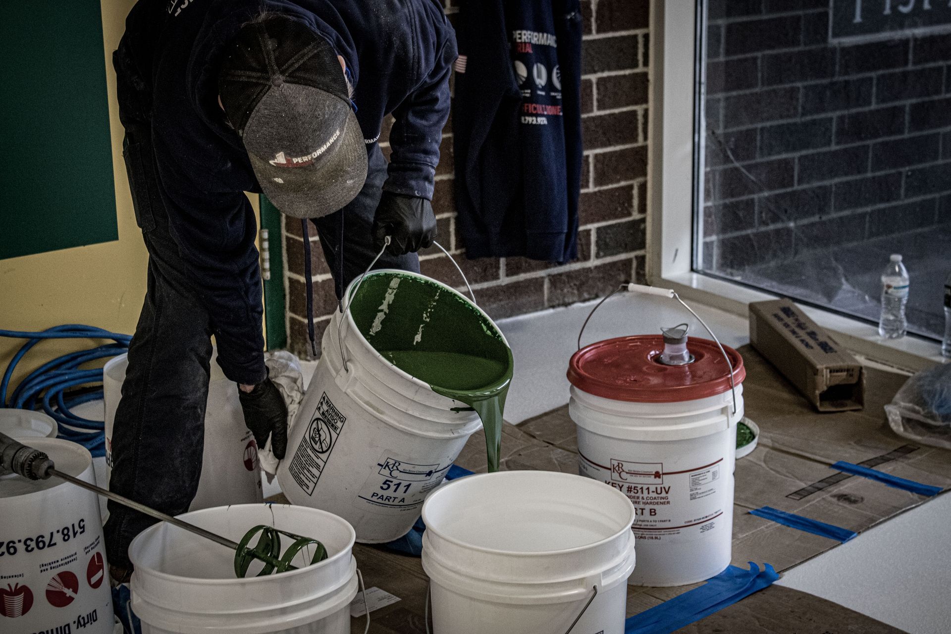 A man is pouring green paint into a white bucket.