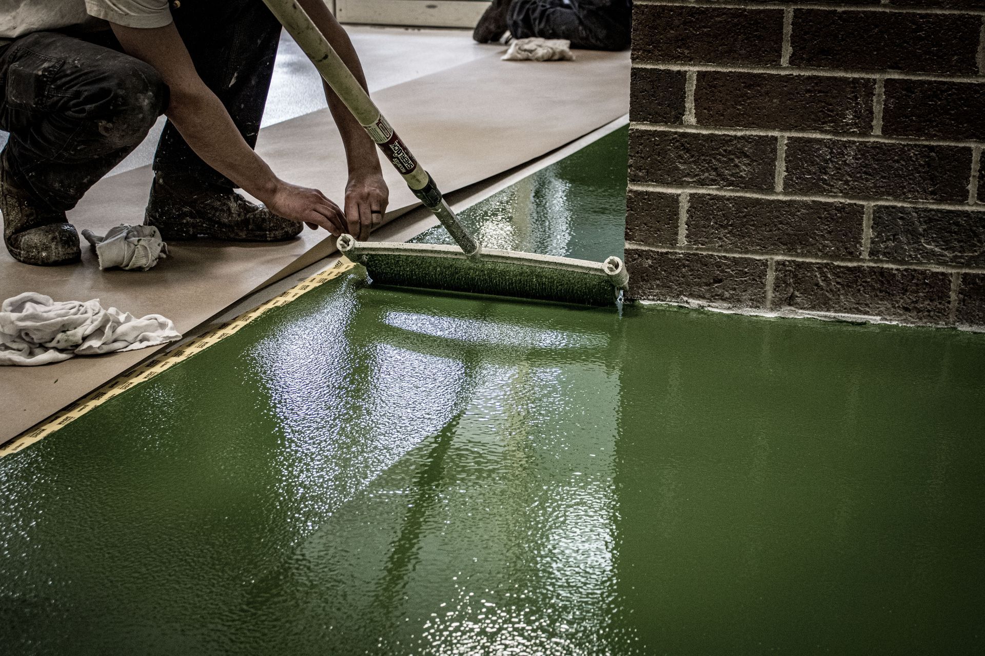 A man is painting a green floor with a roller.