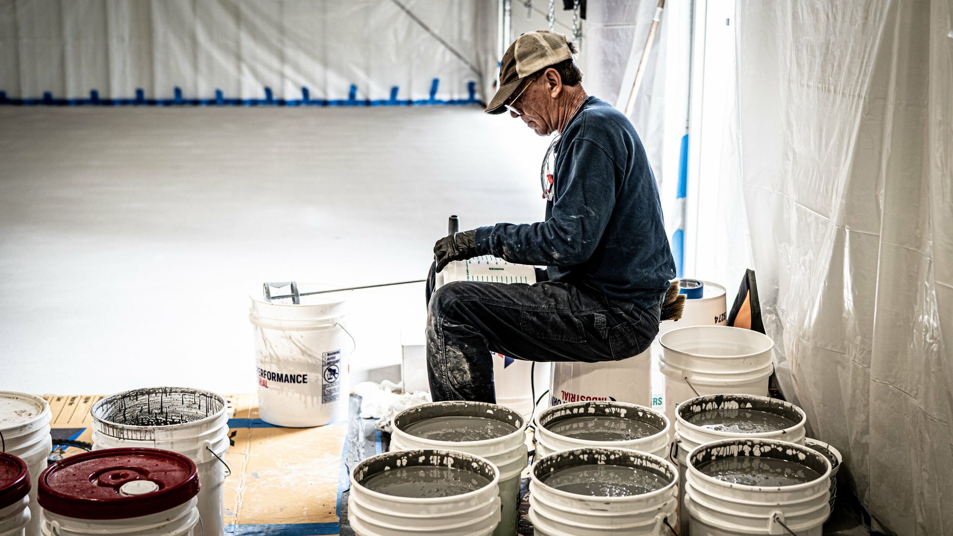 A man is sitting on a pile of buckets in a room.