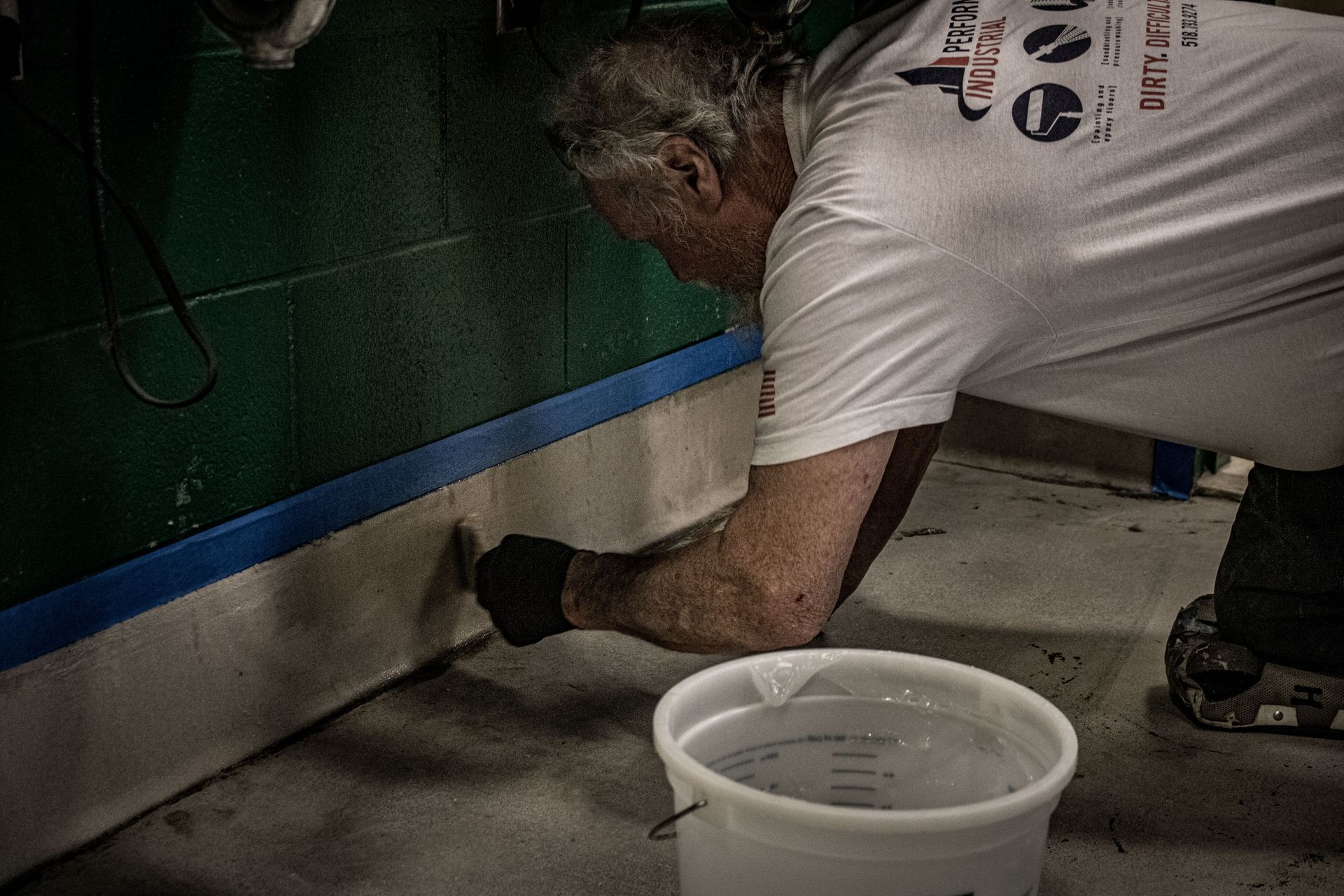 A man is painting a wall next to a bucket of water.