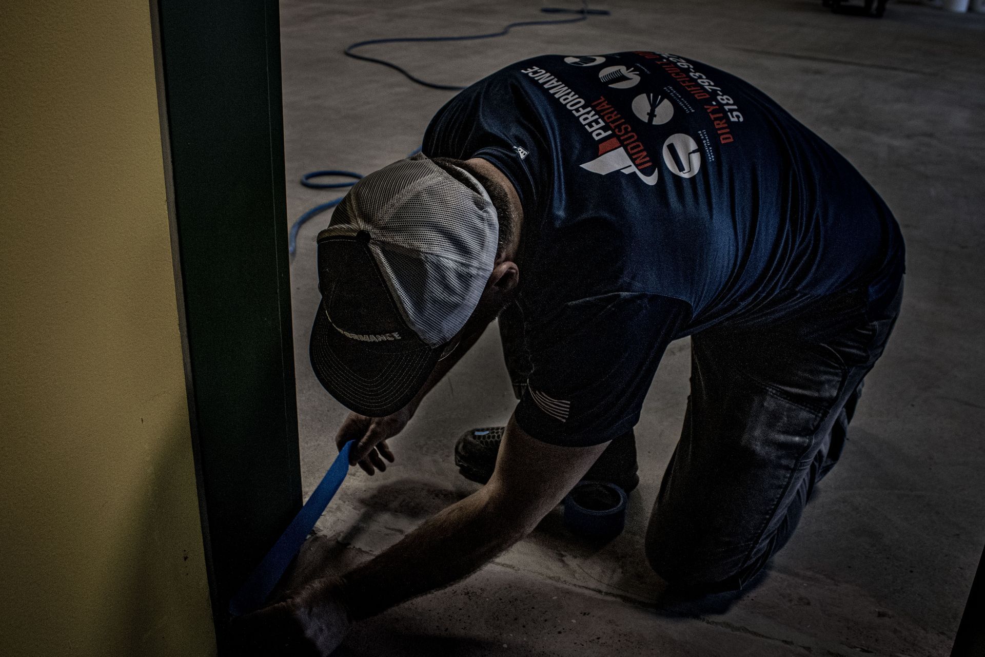 A man in a blue shirt is kneeling down and working on the floor.