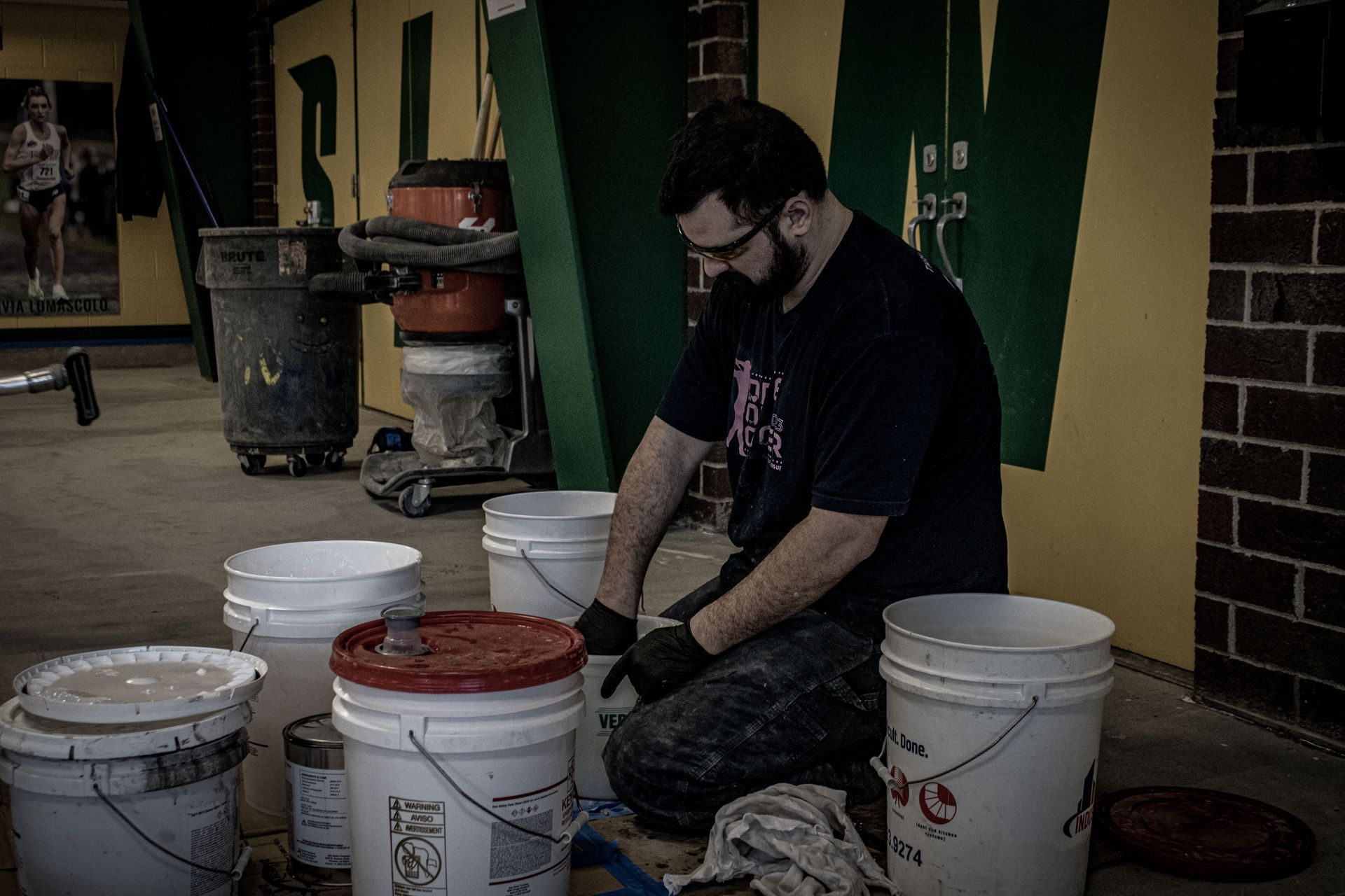 A man is kneeling down next to buckets of paint.