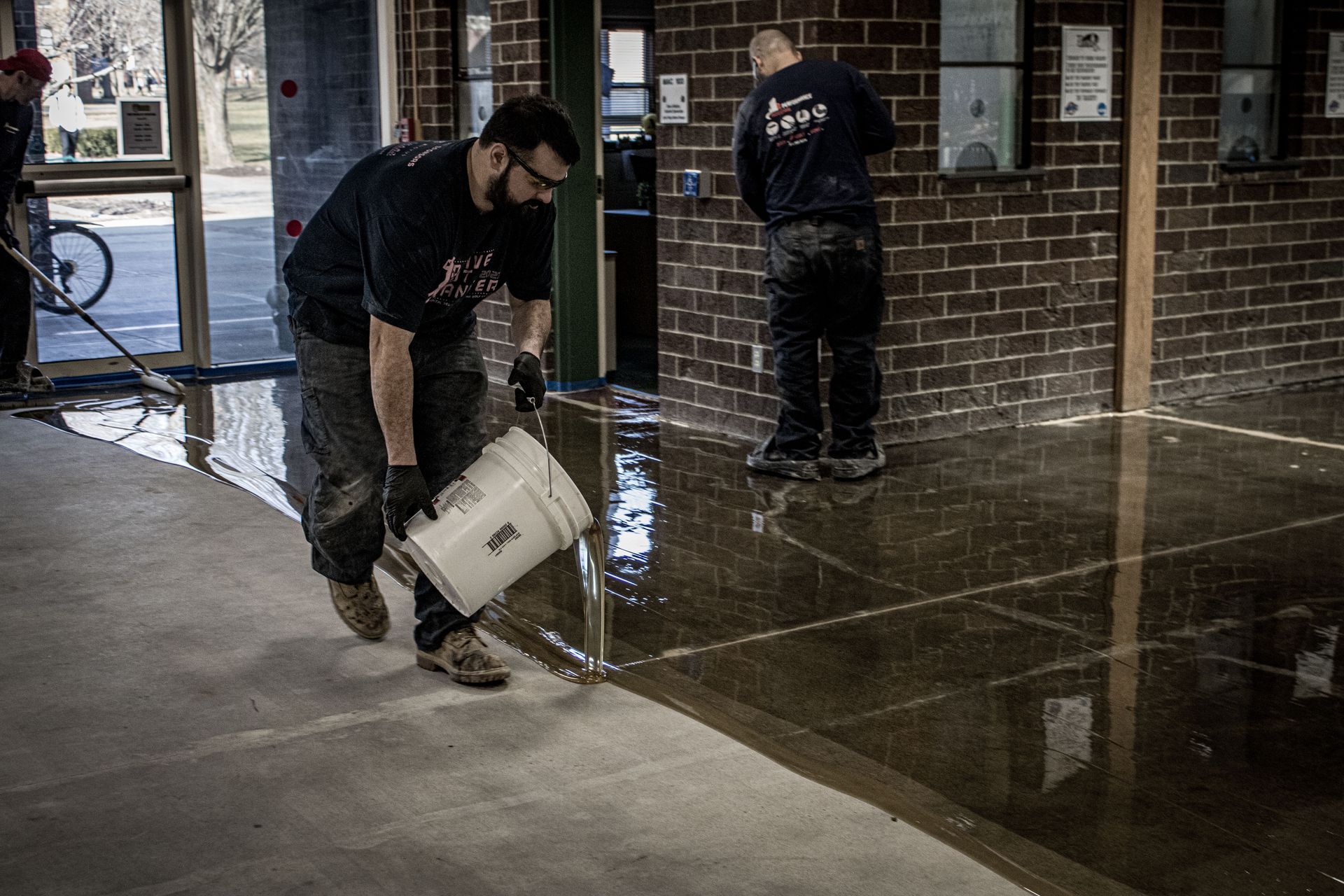 A man is pouring a bucket of liquid on a concrete floor.