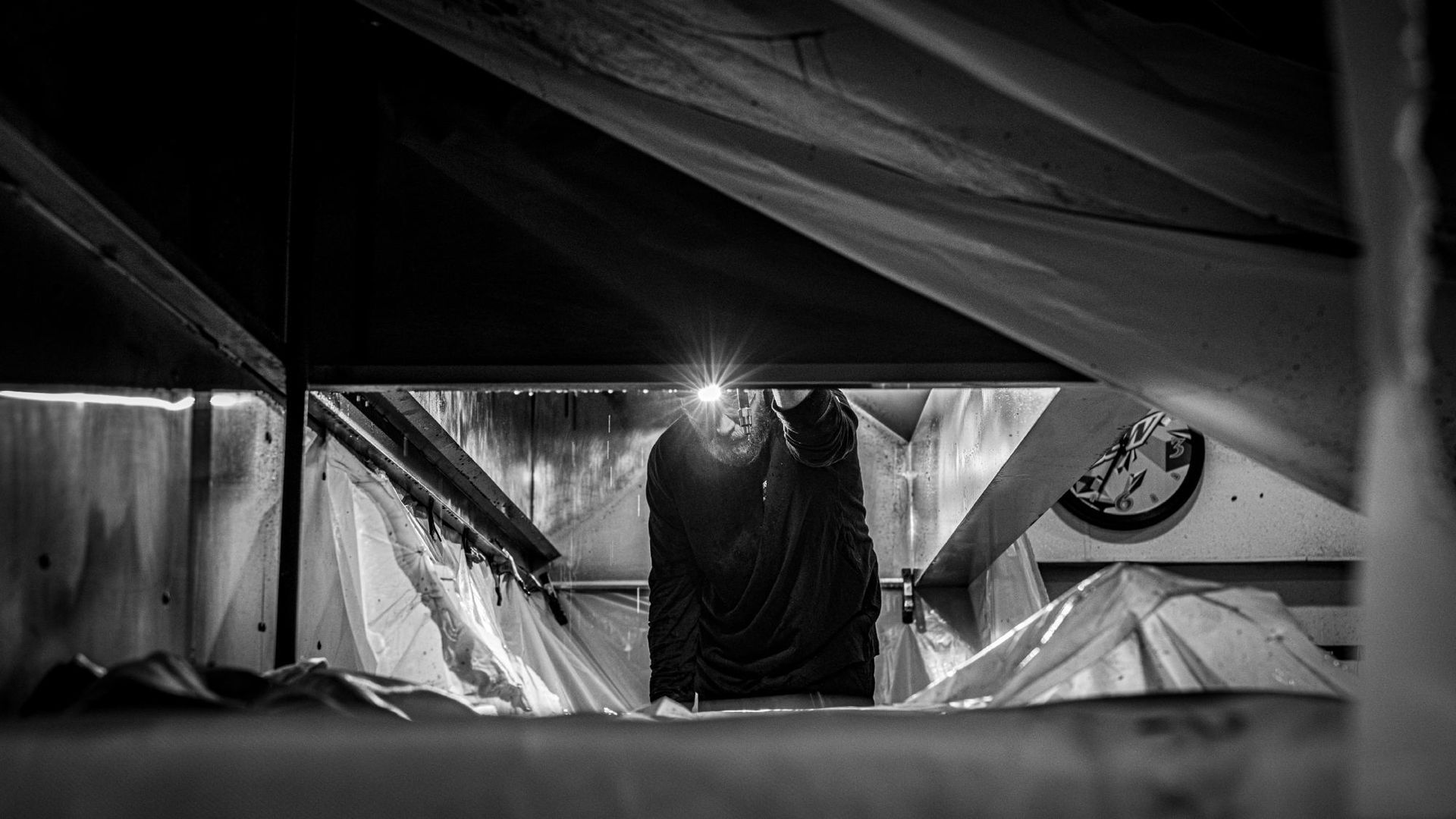 A black and white photo of a person looking under a ceiling with a flashlight.