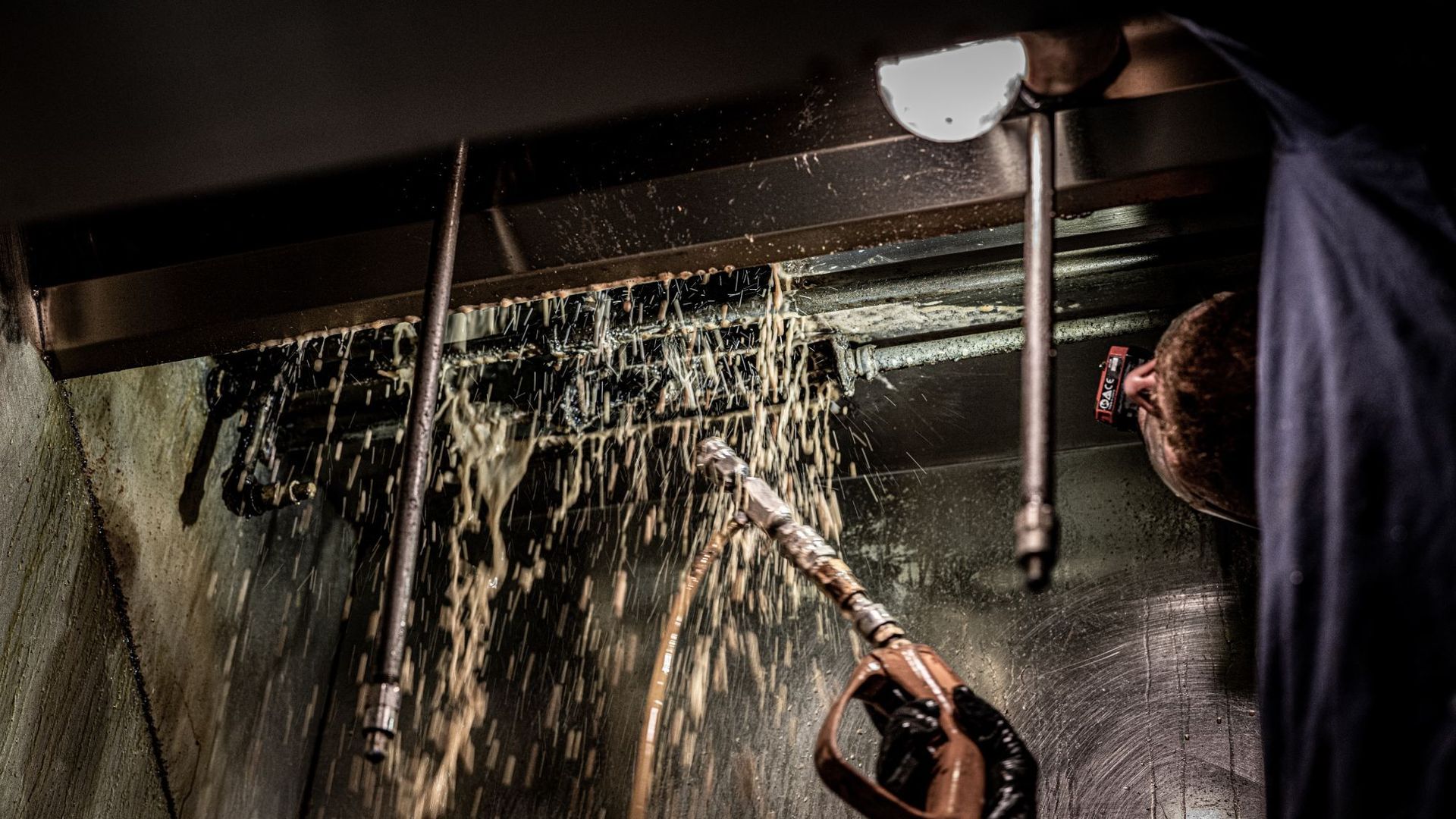A man is cleaning a drain with a hose in a dark room.
